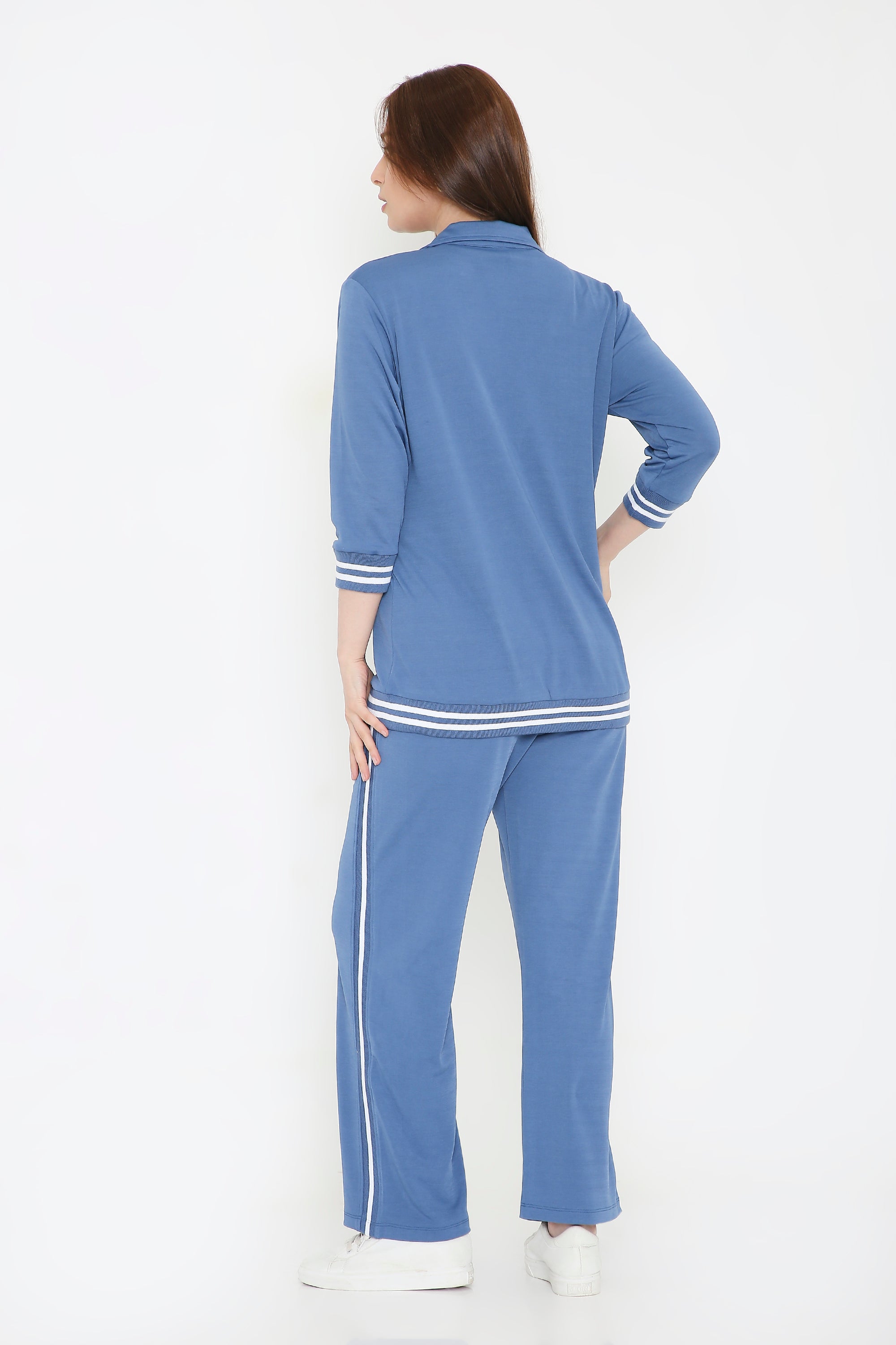 A woman faces away in the Atlantic Blue Athleisure Blazer Jacket and Track Set, featuring white stripes, against a white background.