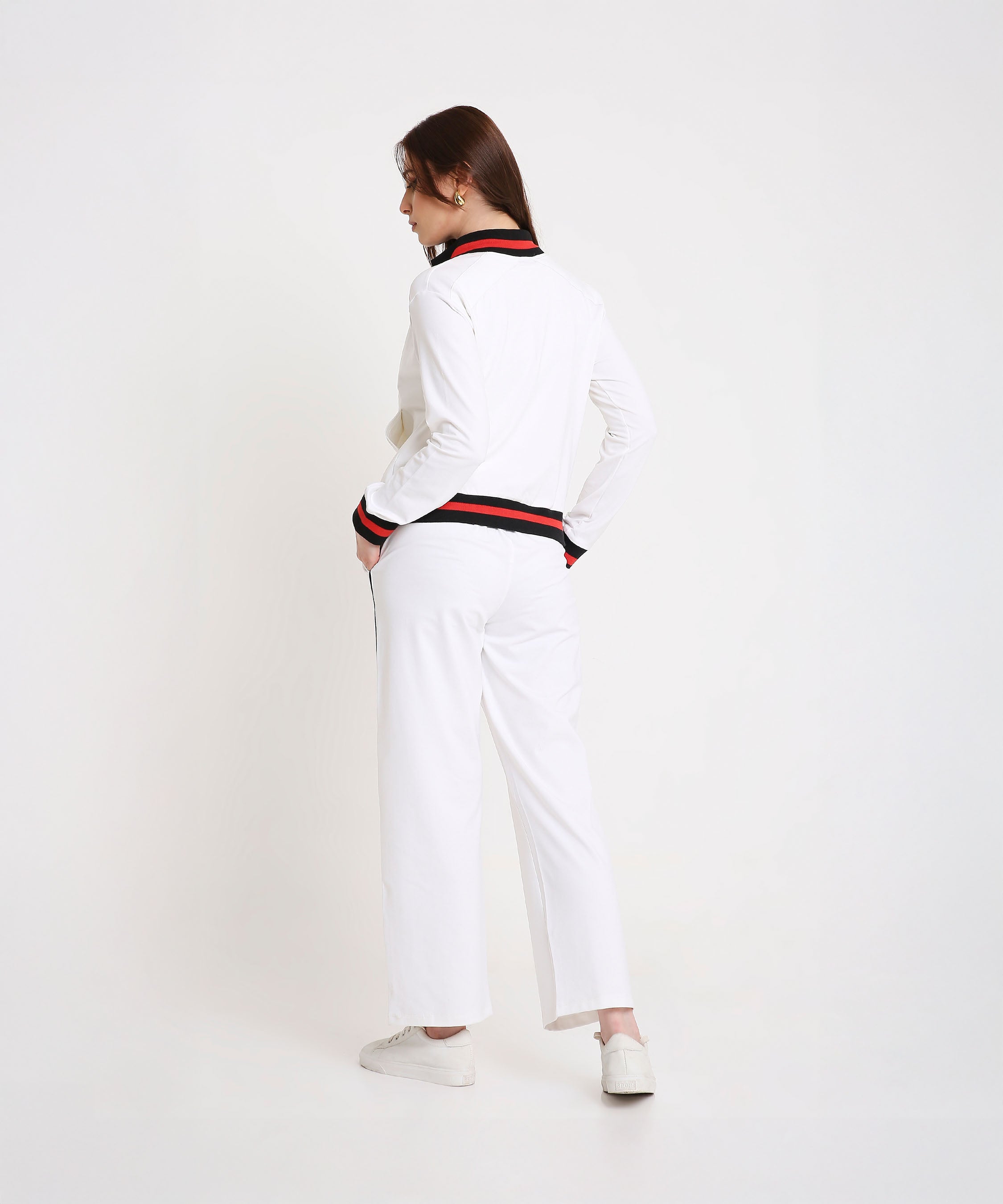 Woman sporting the Two Piece Bold Contrast White Tracksuit, featuring black and red trim on cotton-blend fabric, hands in pockets and facing away for a chic, modern look.