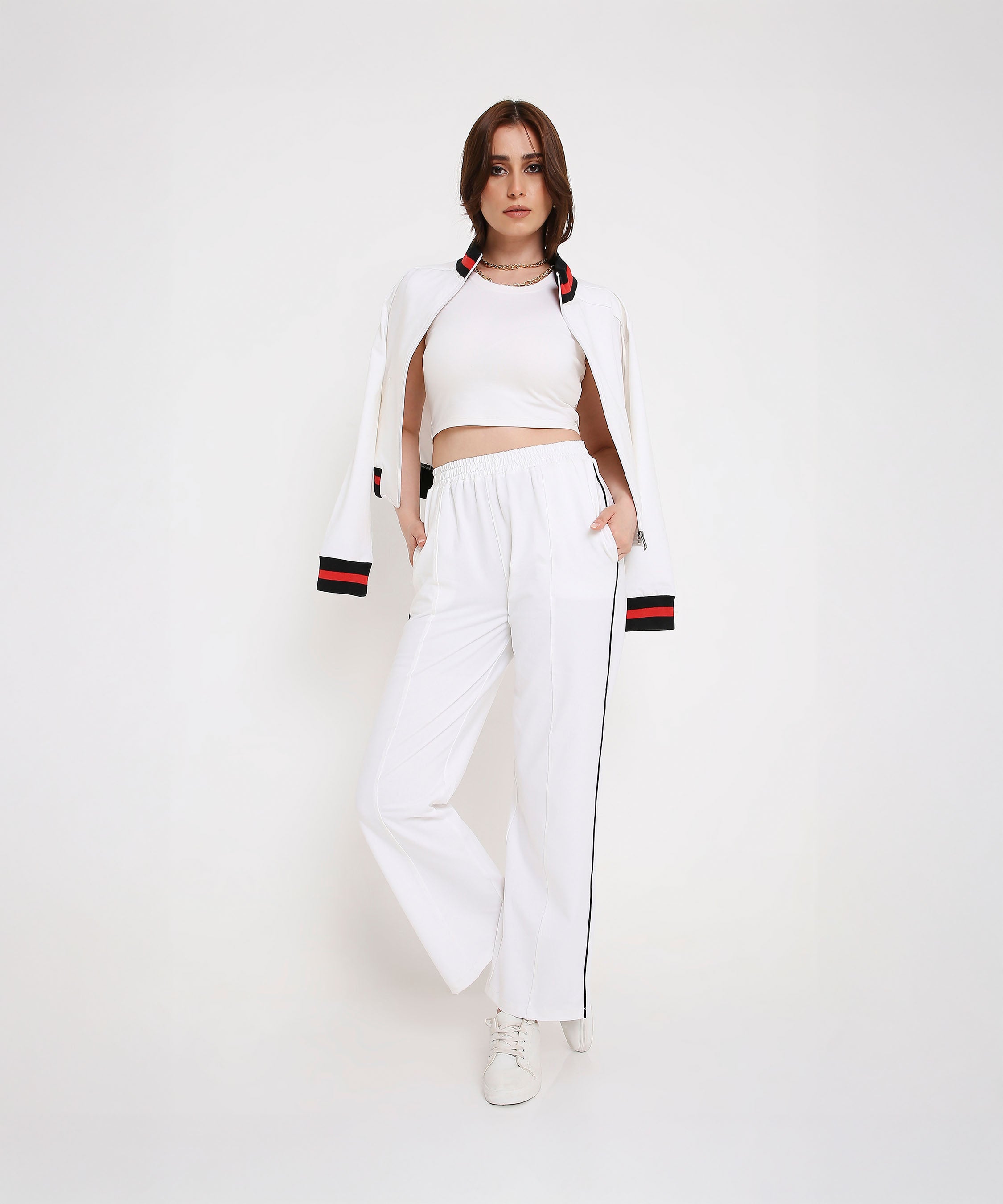Woman in a sporty-chic look, wearing the Two Piece Bold Contrast White Tracksuit—white crop top and matching jacket with black striped pants—stands against a white background.