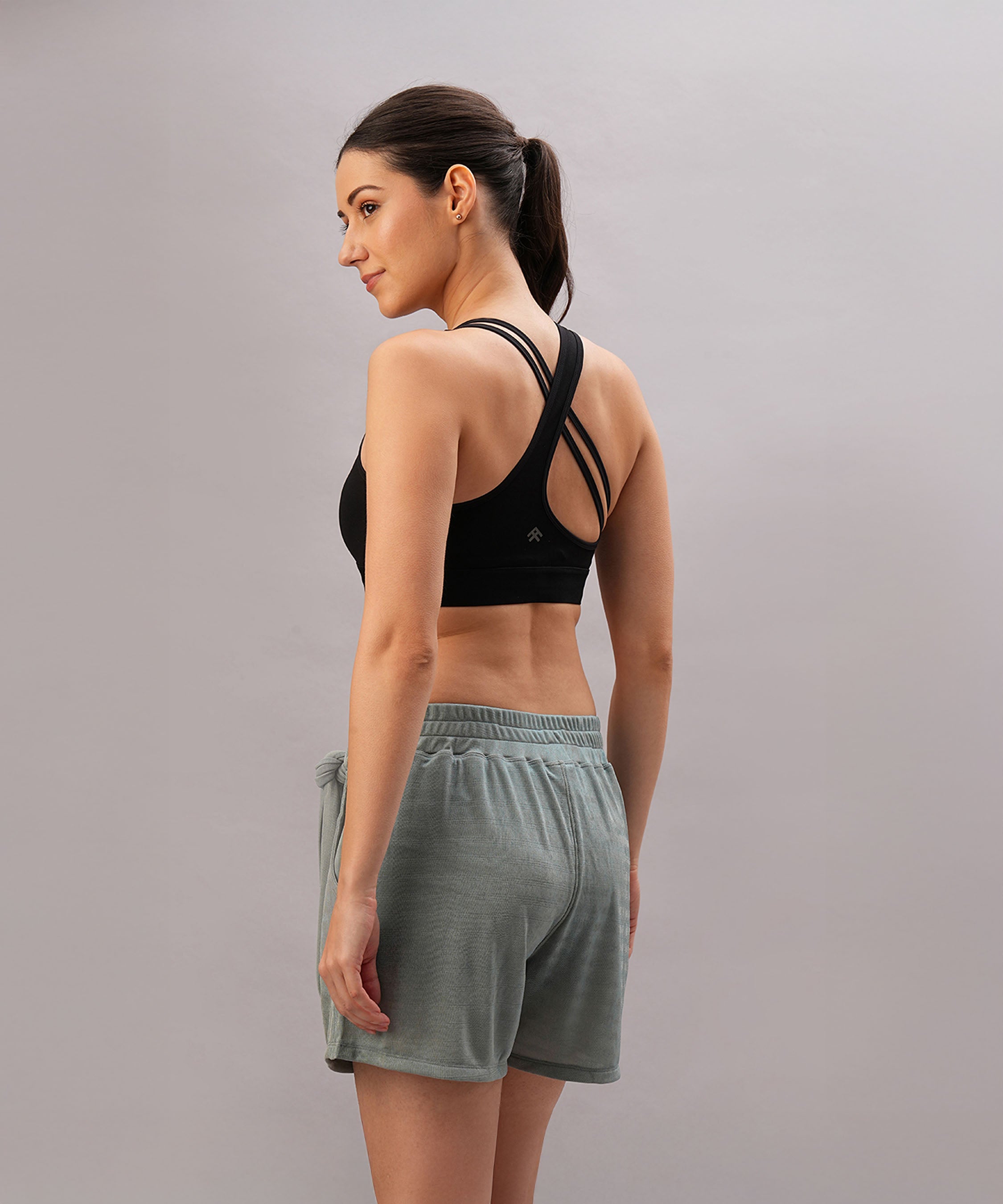 A woman wearing the Black Sports Bra with adjustable straps and gray shorts stands sideways, looking over her shoulder.