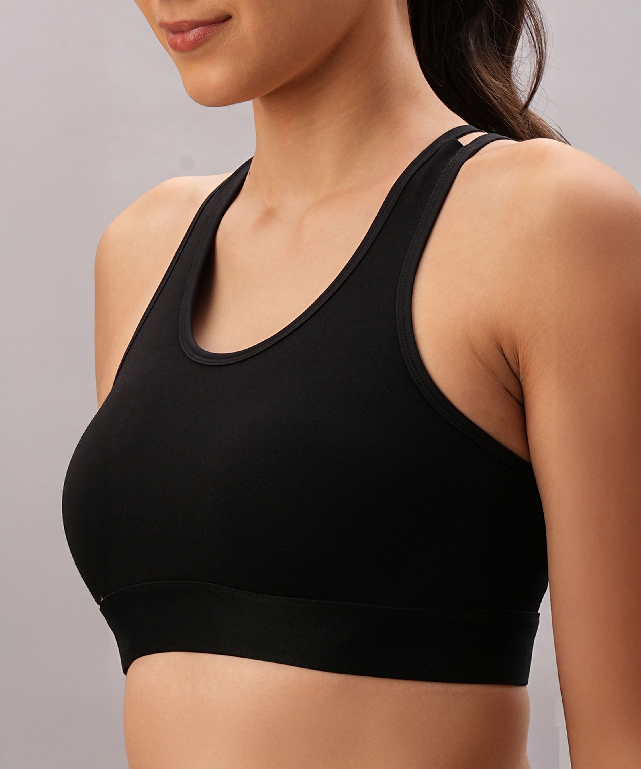 A woman models the Black Sports Bra, featuring adjustable straps, shown from shoulders to midriff against a plain background.