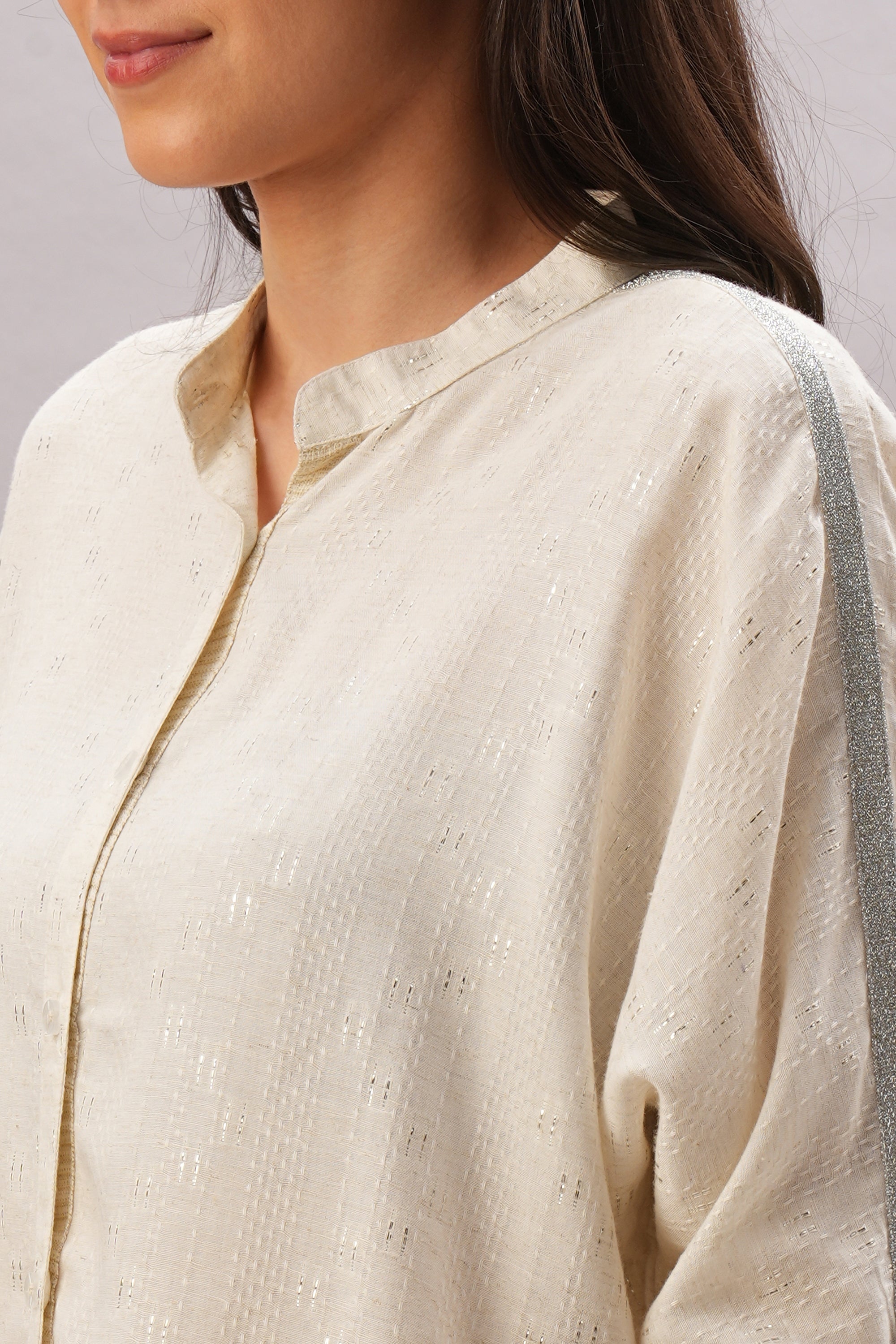 A woman models the Beige Linen Set—a cream-colored, textured top with a metallic shoulder stripe—showcasing effortless style and breathable comfort in one chic look.