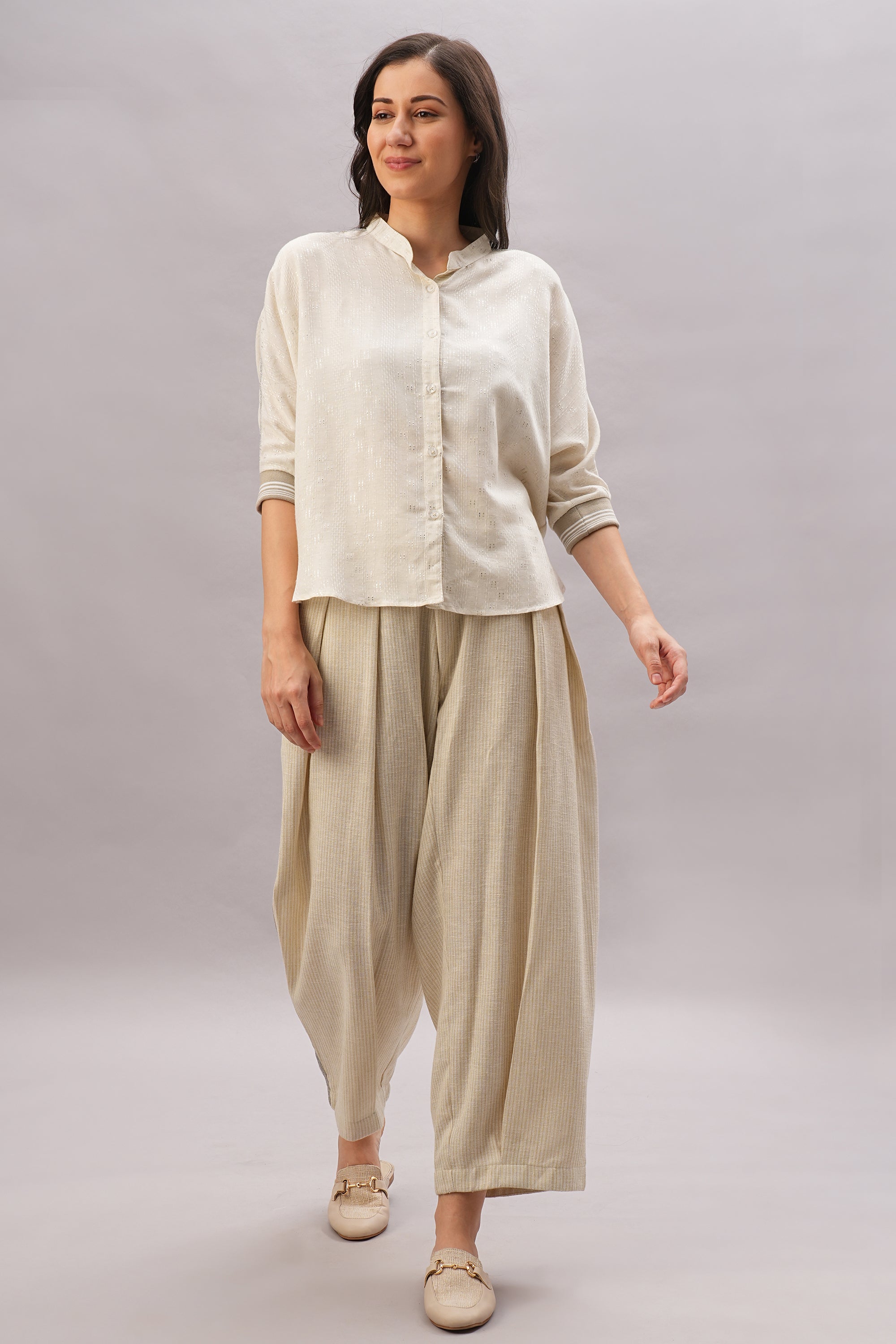 A woman smiles in an effortless style, wearing the Beige Linen Set—featuring a loose, cream-colored shirt and wide, pleated beige pants crafted from breathable linen.