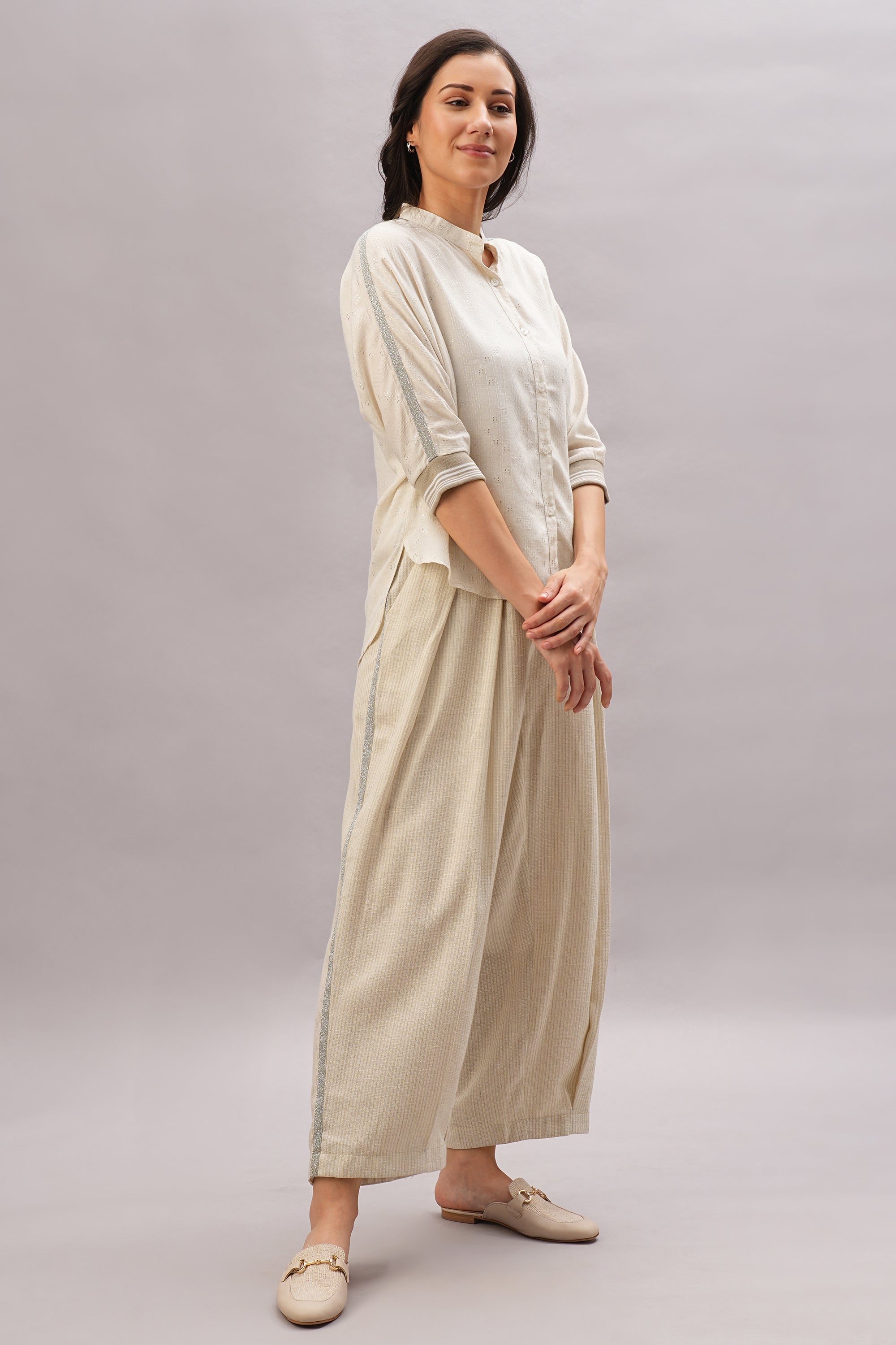 A woman smiles with hands clasped, wearing the Beige Linen Set and loafers on a plain background—highlighting effortless style and the breathable comfort of linen.