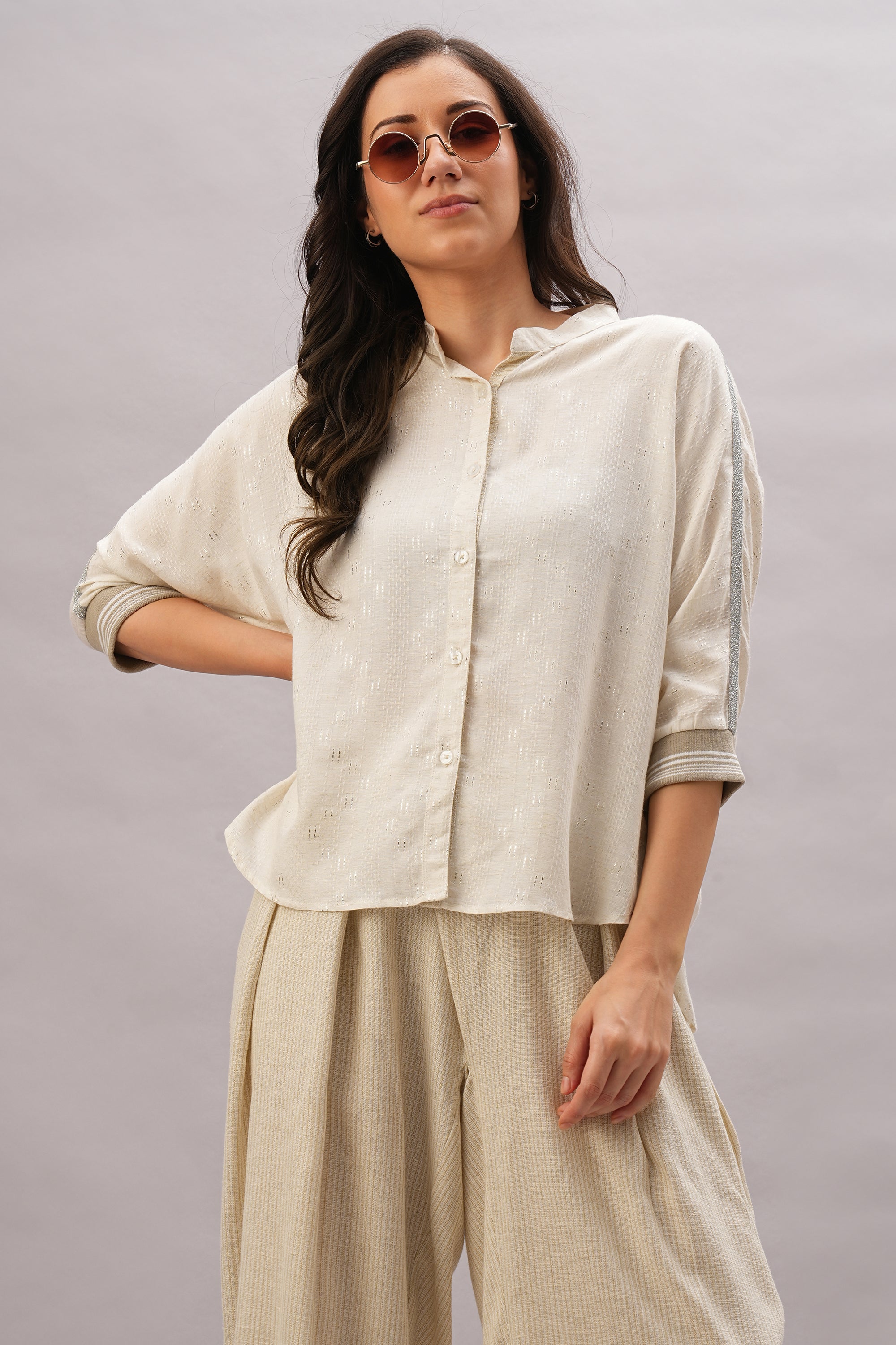 A woman models the Beige Linen Set—sunglasses, loose cream button-up, and wide-leg beige pants—for an effortless, breathable style. This look highlights the relaxed appeal of linen against a neutral backdrop.