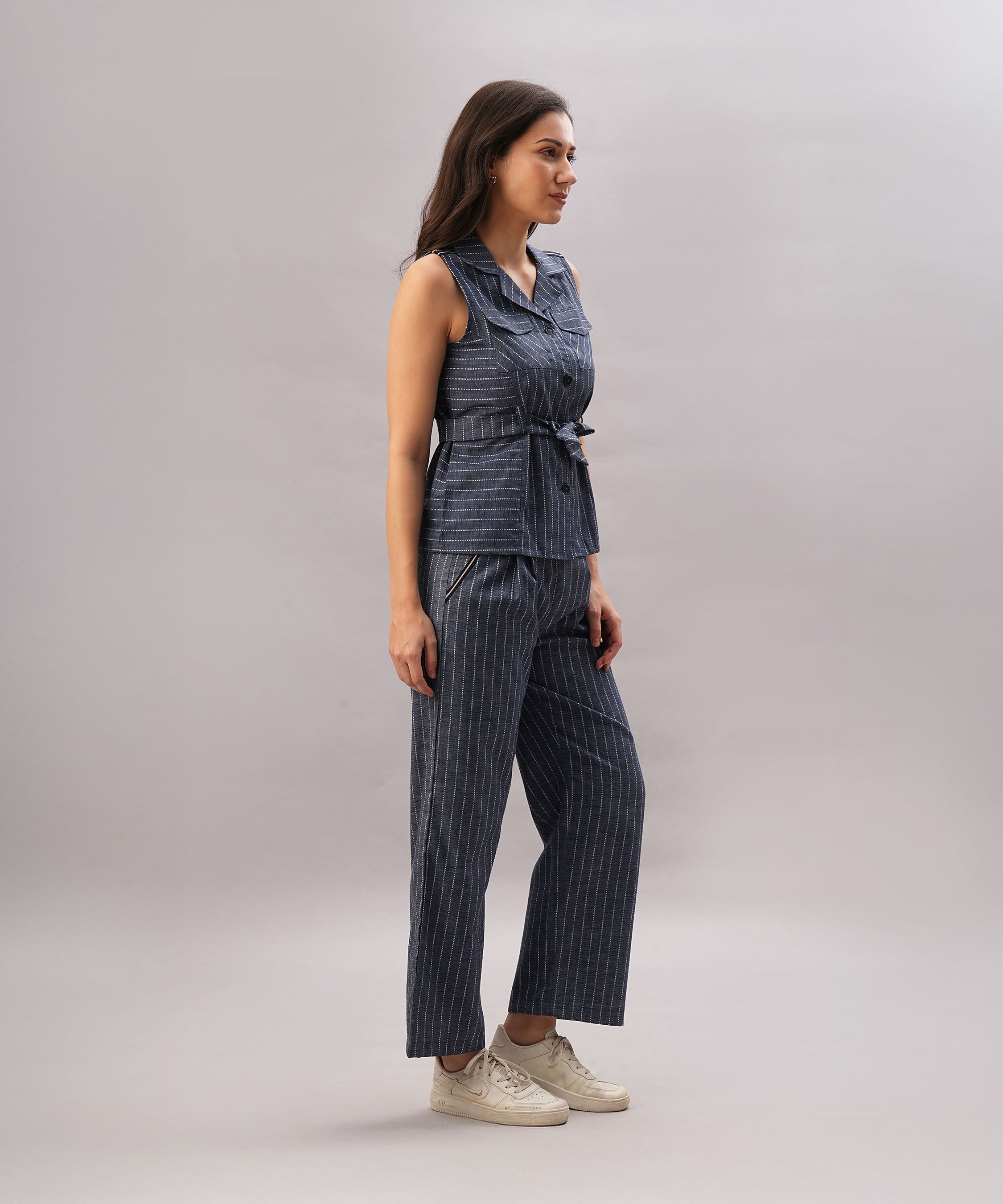 A woman wearing the Navy Blue Stripe Set stands sideways in white sneakers, showcasing its sleeveless design and comfortable fit.