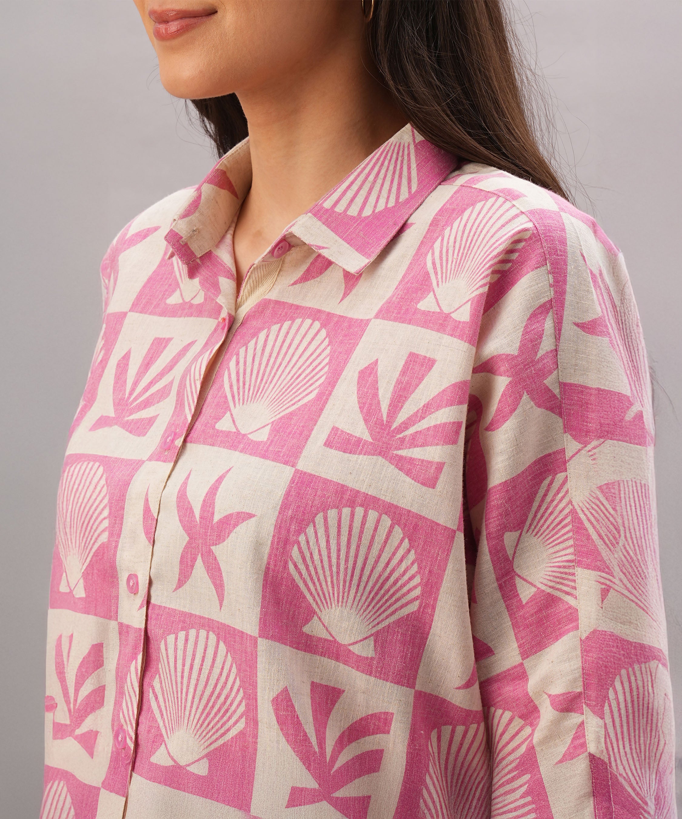 A woman models the Pink Co-Ord set, featuring a stylish shirt in pink and beige with seashell and leaf patterns, shown from the shoulders up.