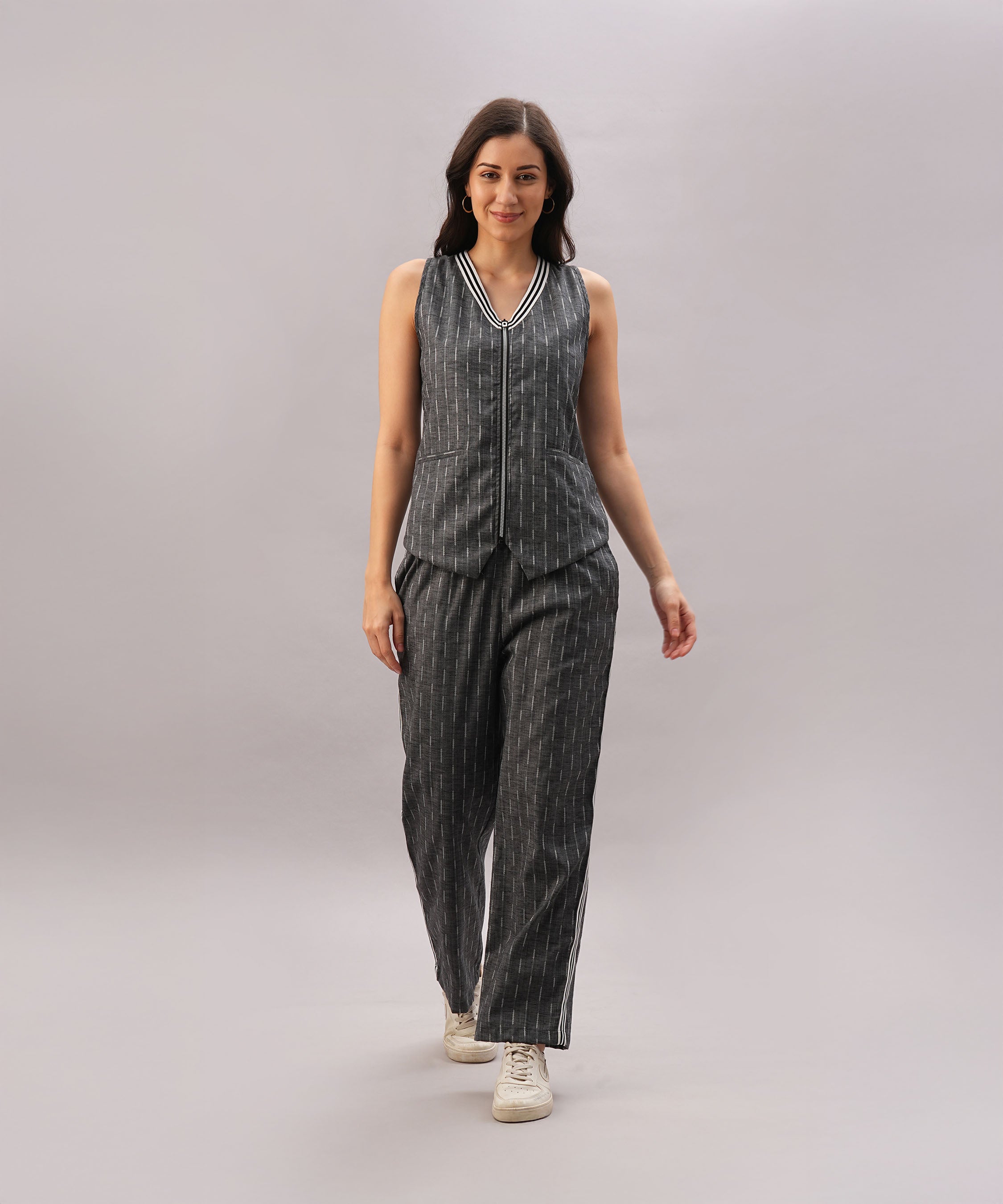 A woman models the Grey Stripes Sleeveless Set with white sneakers, walking against a plain light gray background.