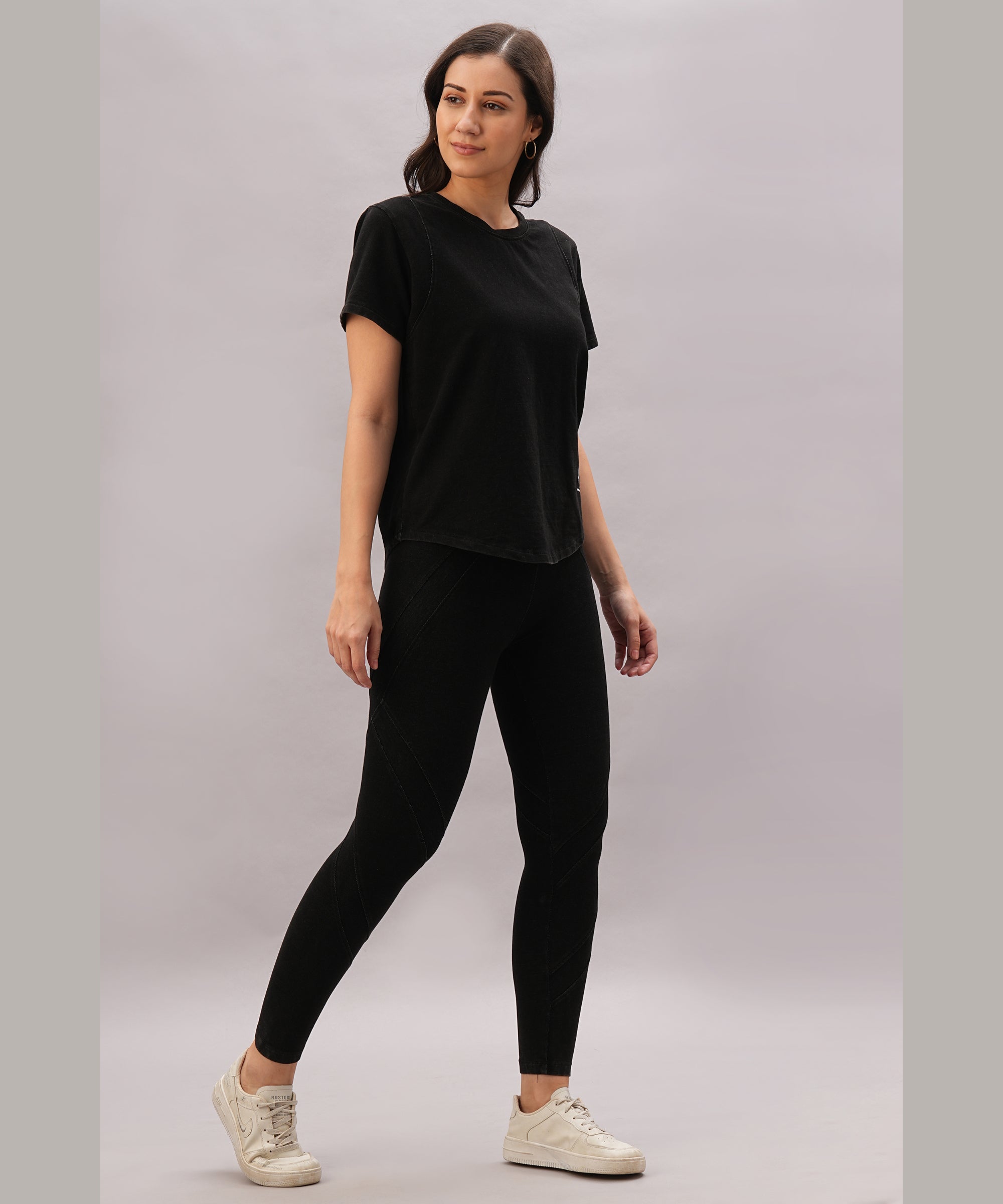 A woman stands against a light gray background wearing white sneakers and Black Denim Wash Leggings featuring a high-rise waistband and four-way stretch fabric, paired with a black t-shirt.
