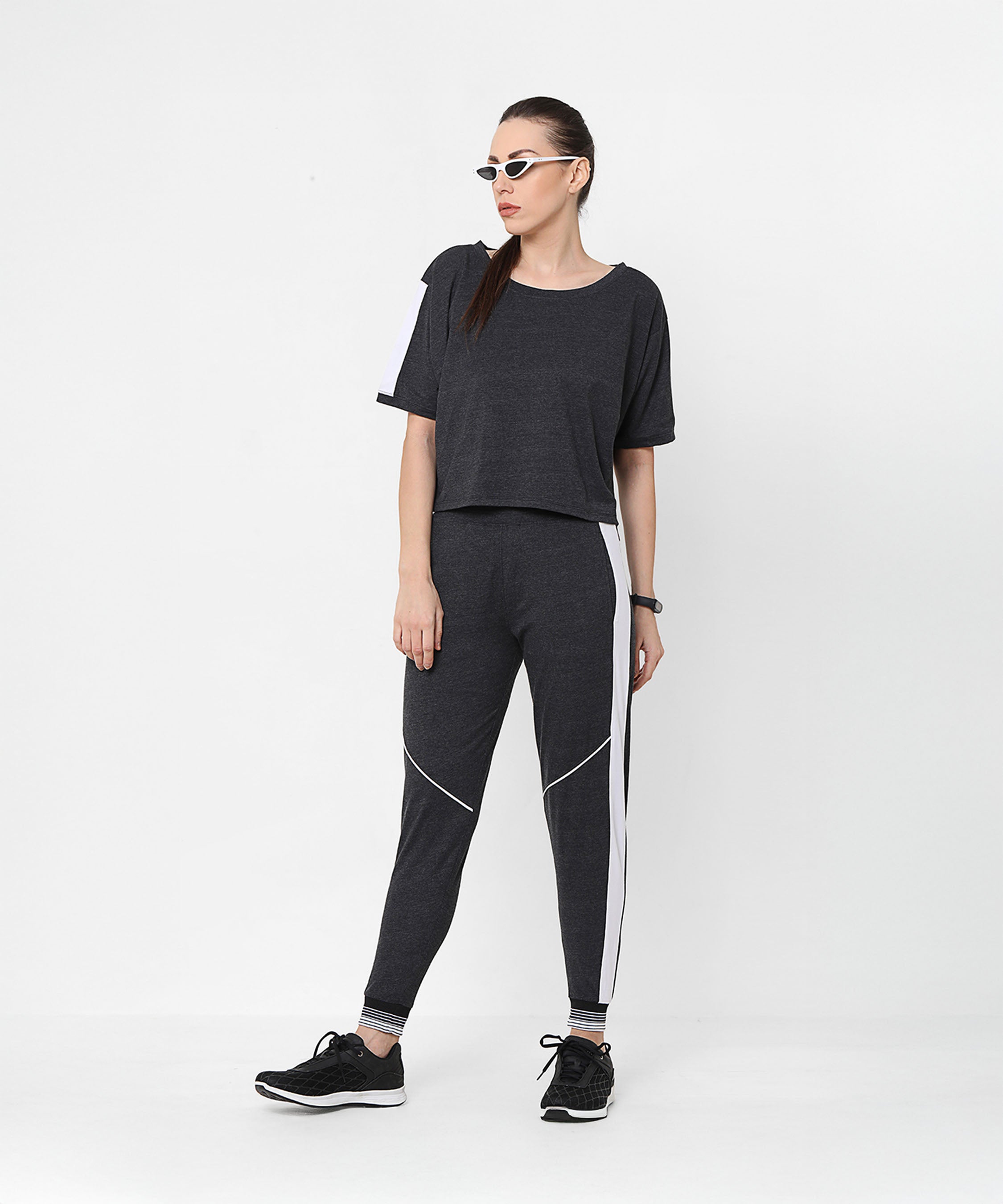 Woman in sunglasses wearing the Melange Dark Grey Set with joggers and a comfort fit top featuring white stripes, standing against a white background.