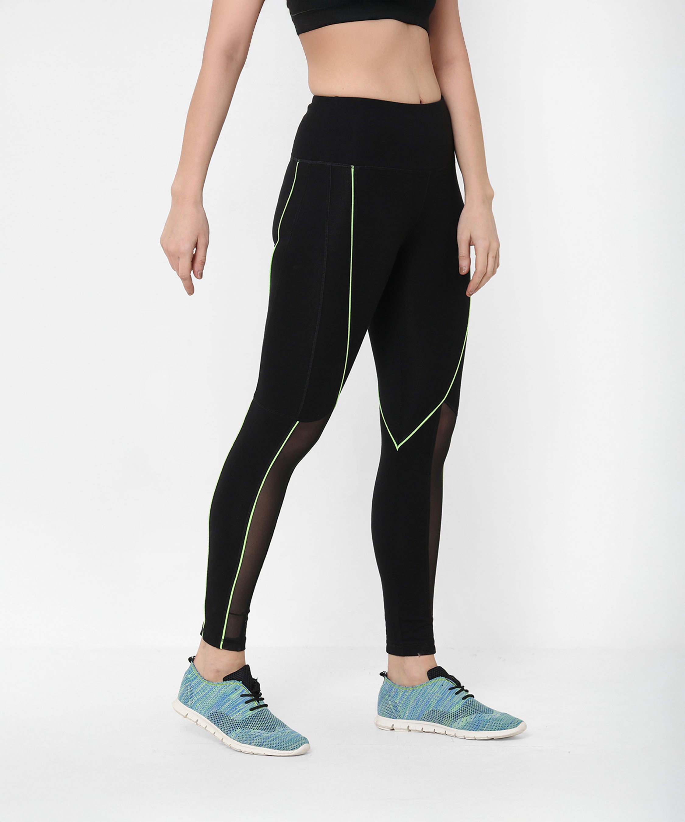 A woman confidently models Fab Fit Neon Pop Leggings with a high-rise waistband, paired with a black crop top and blue sneakers, against a white background.