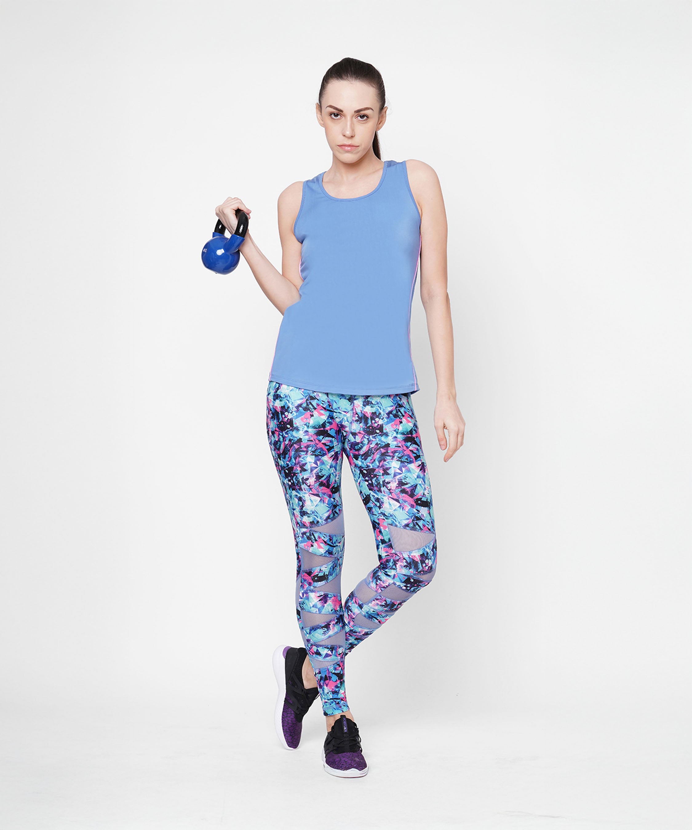 Woman in Nyla racer back top and colorful leggings with an athletic look, holding a small kettlebell against a white background.