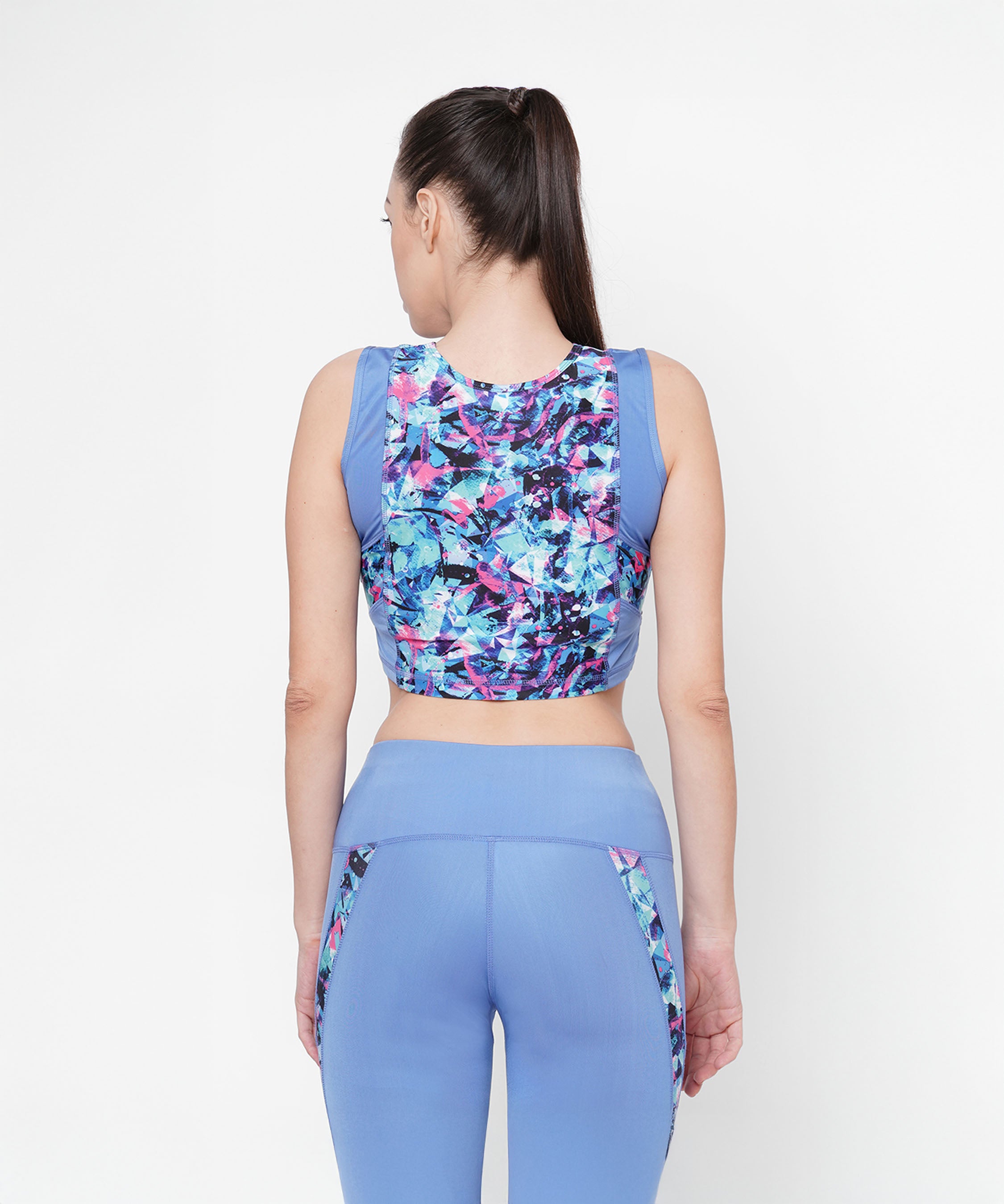 Woman wearing the Lia Crop Top in blue workout wear, showcasing a colorful geometric back design—ideal for an active lifestyle.