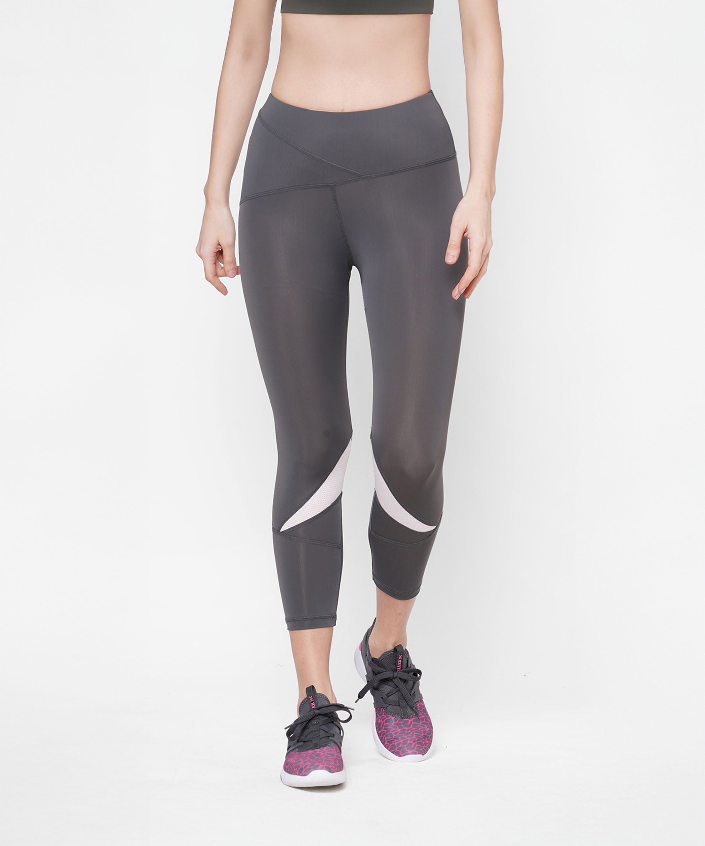 Woman wearing Classic Capri dark gray high-waisted leggings with a thick waistband and white accents, paired with pink sneakers, standing against a white background.