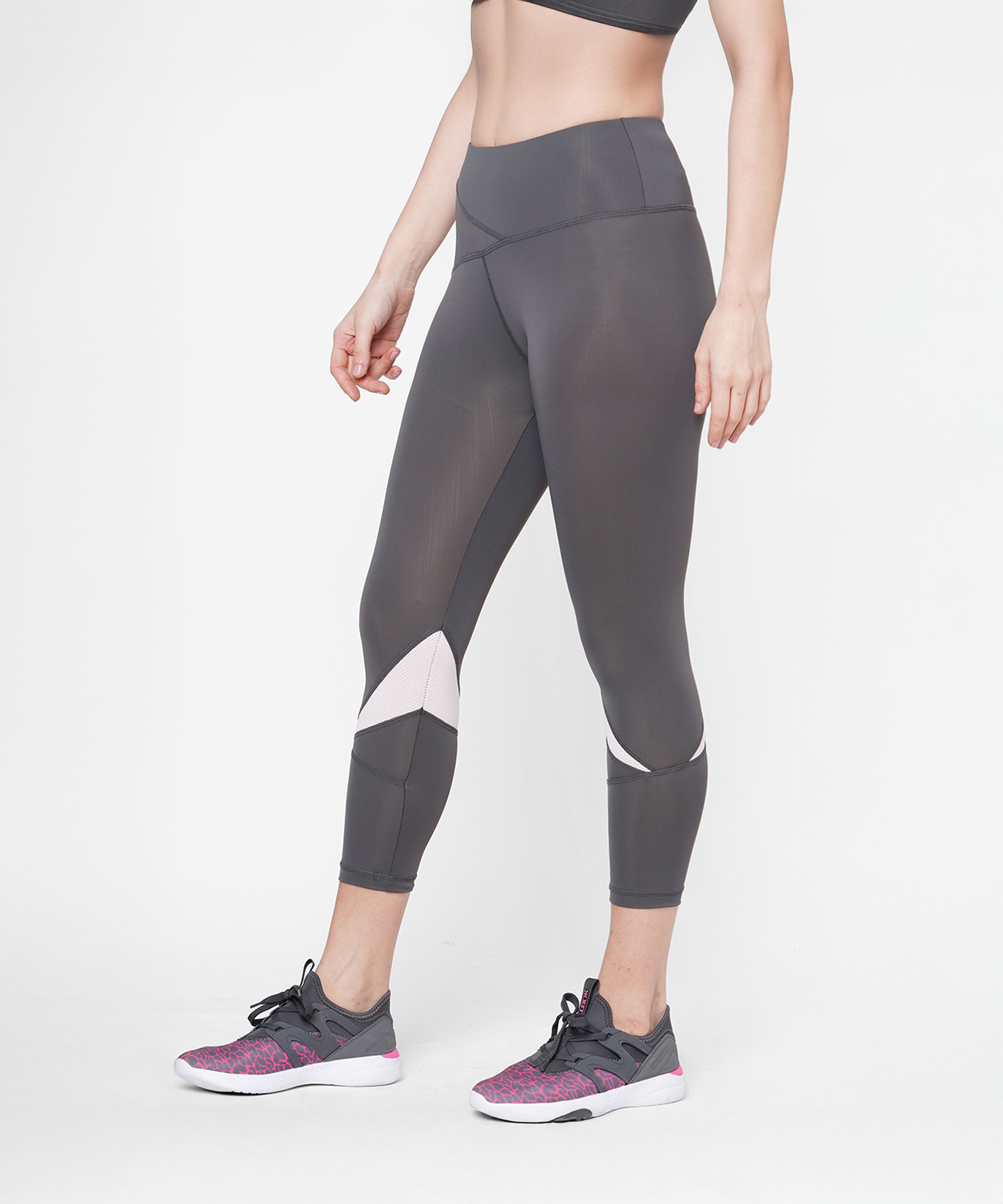 A woman wearing the Classic Capri in grey with a thick waistband, paired with a sports bra and pink athletic shoes, stands against a white background.