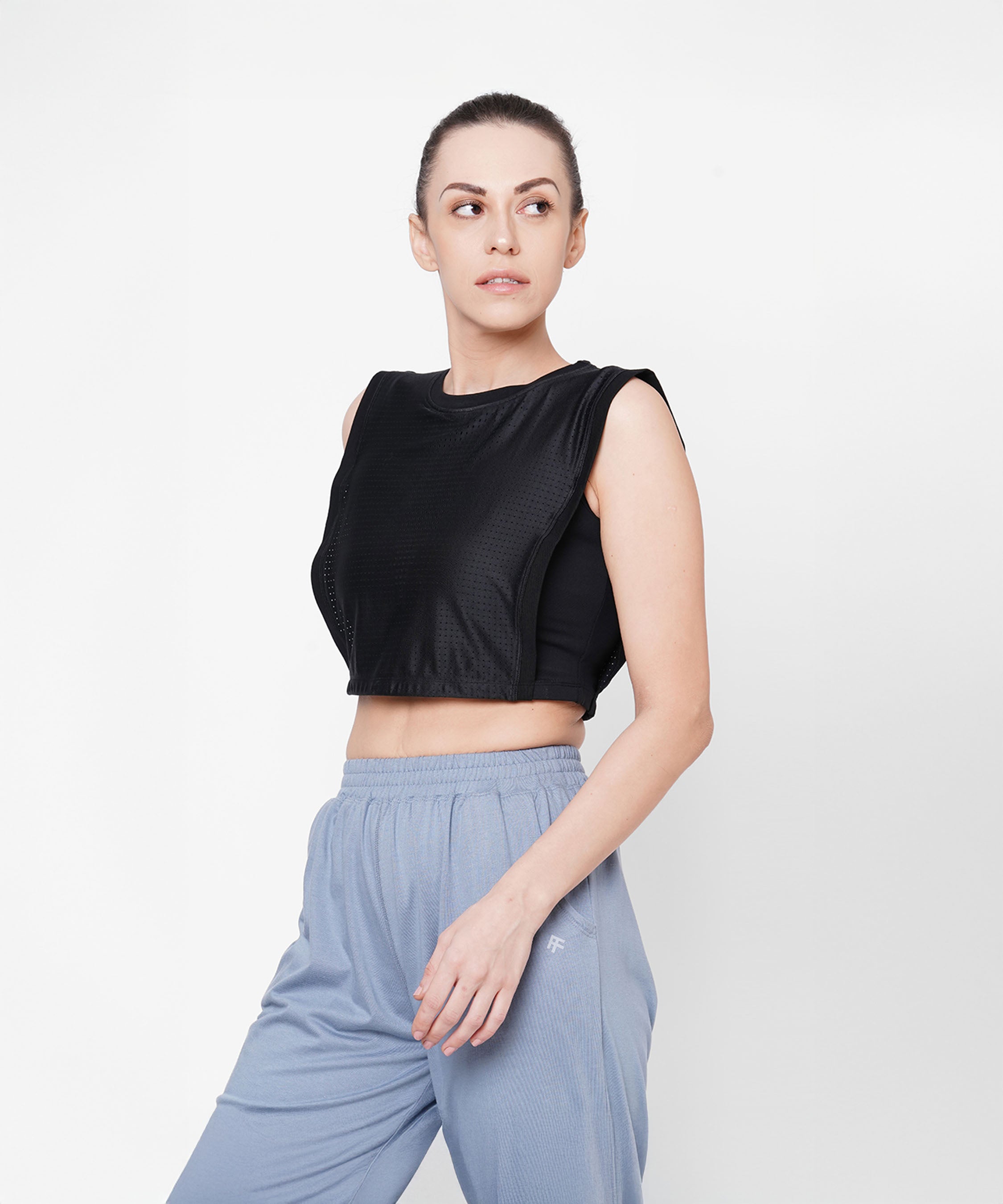 Woman in athletic wear looks to the side, wearing the Black Crop Top With Mesh Overlay and light blue pants against a white background.