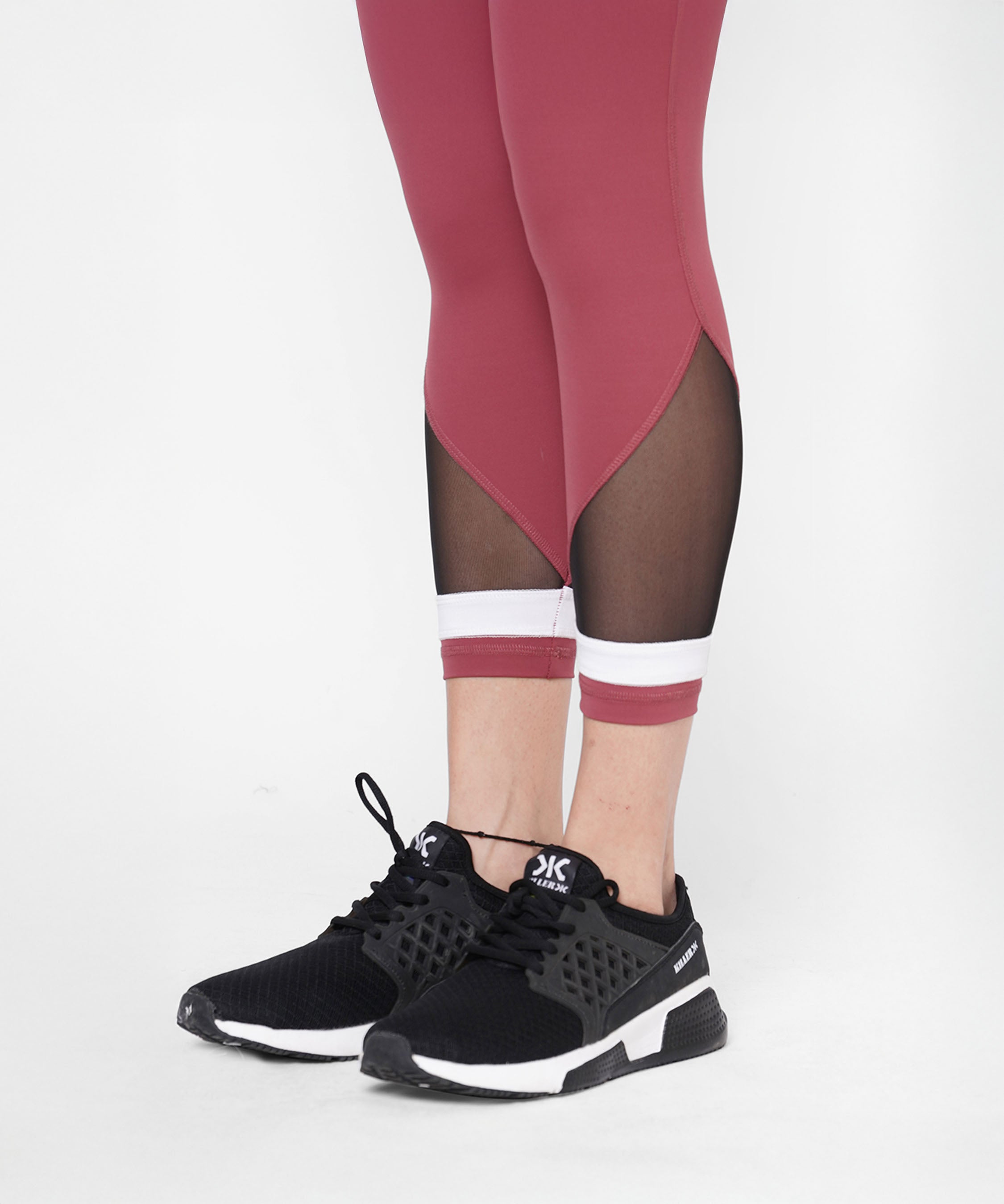 A person wearing Punch pink Capri workout pants with a compression fit waistband and mesh panels, paired with black athletic shoes, stands against a white background.