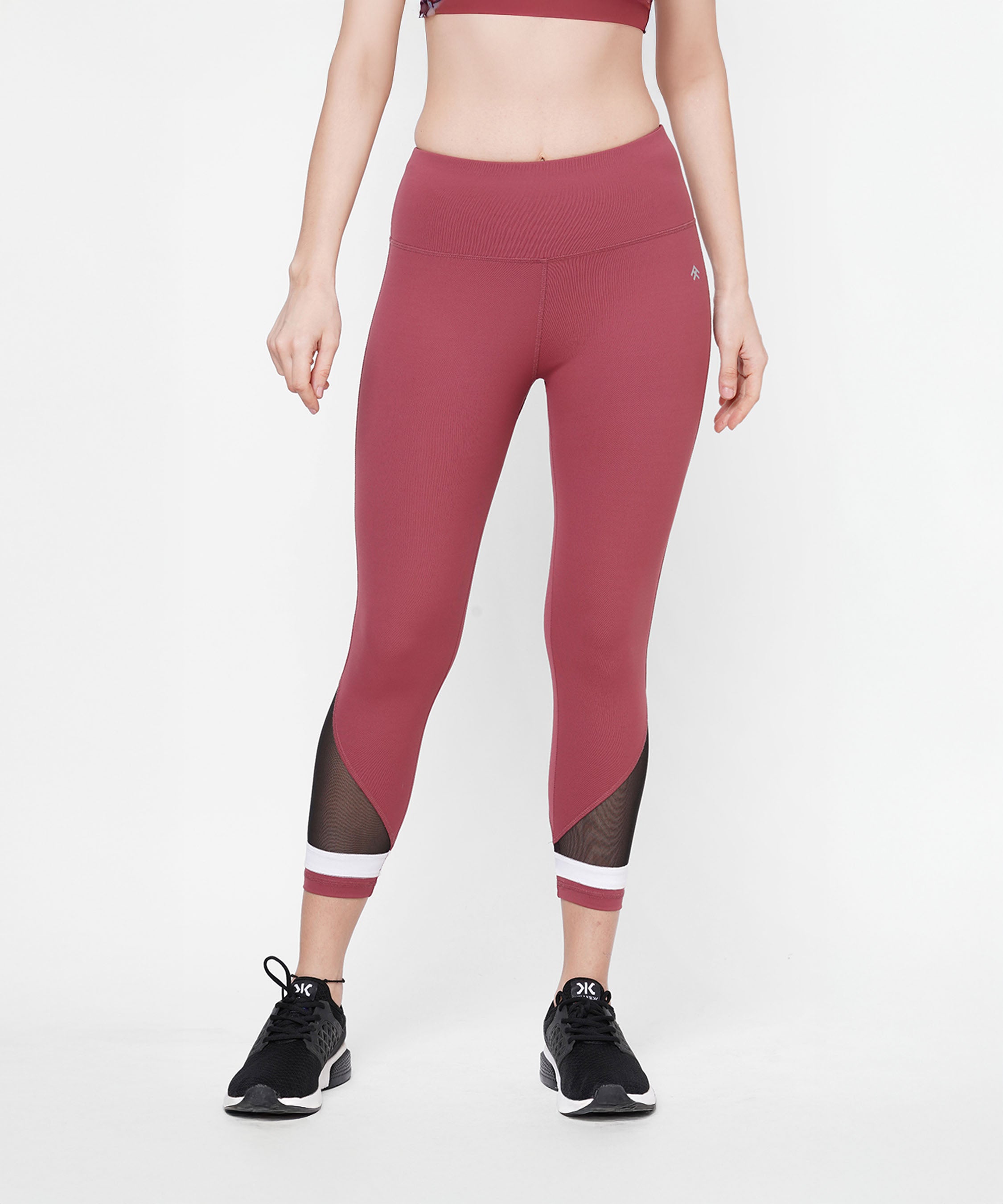 Woman wearing Punch Pink Capri workout pants with a high waist and black mesh panels, featuring a compression fit waistband and paired with black sneakers, standing against a white background.