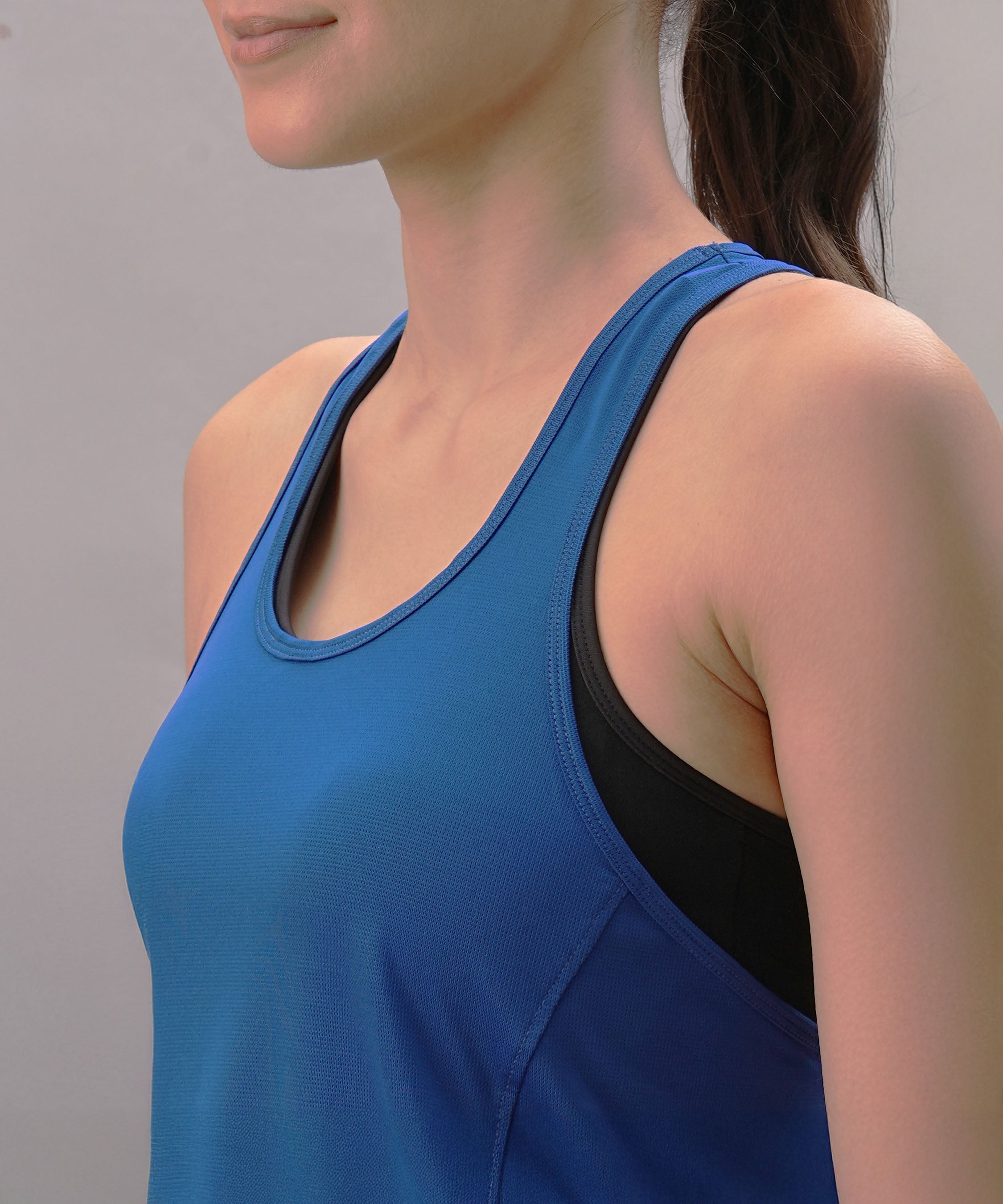 A woman models the Blue Racer Back Top with a black sports bra underneath, standing against a plain background and highlighting this stylish activewear piece.