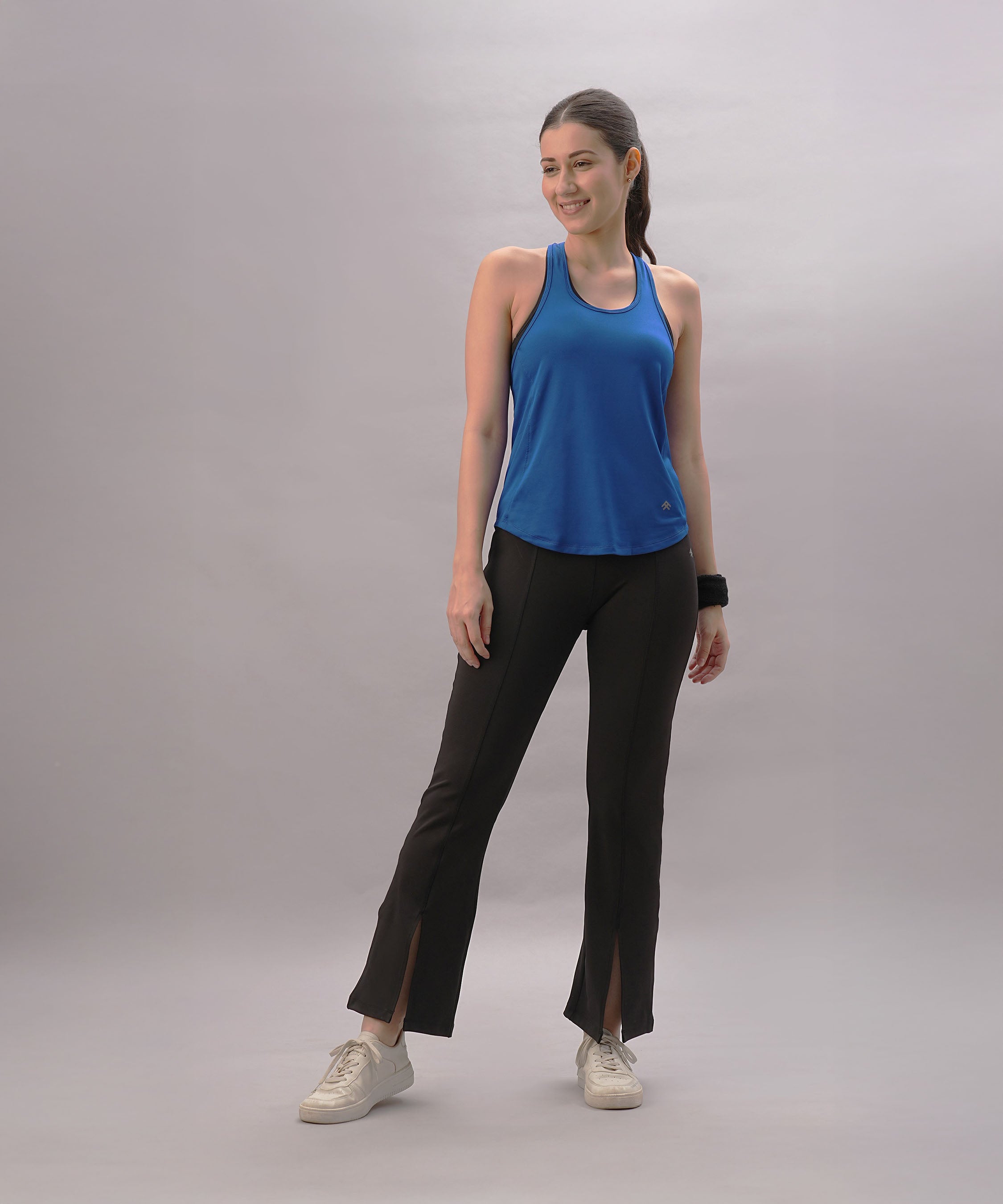 Smiling woman wears a Blue Racer Back Top and black slit-hem pants against a plain light background.