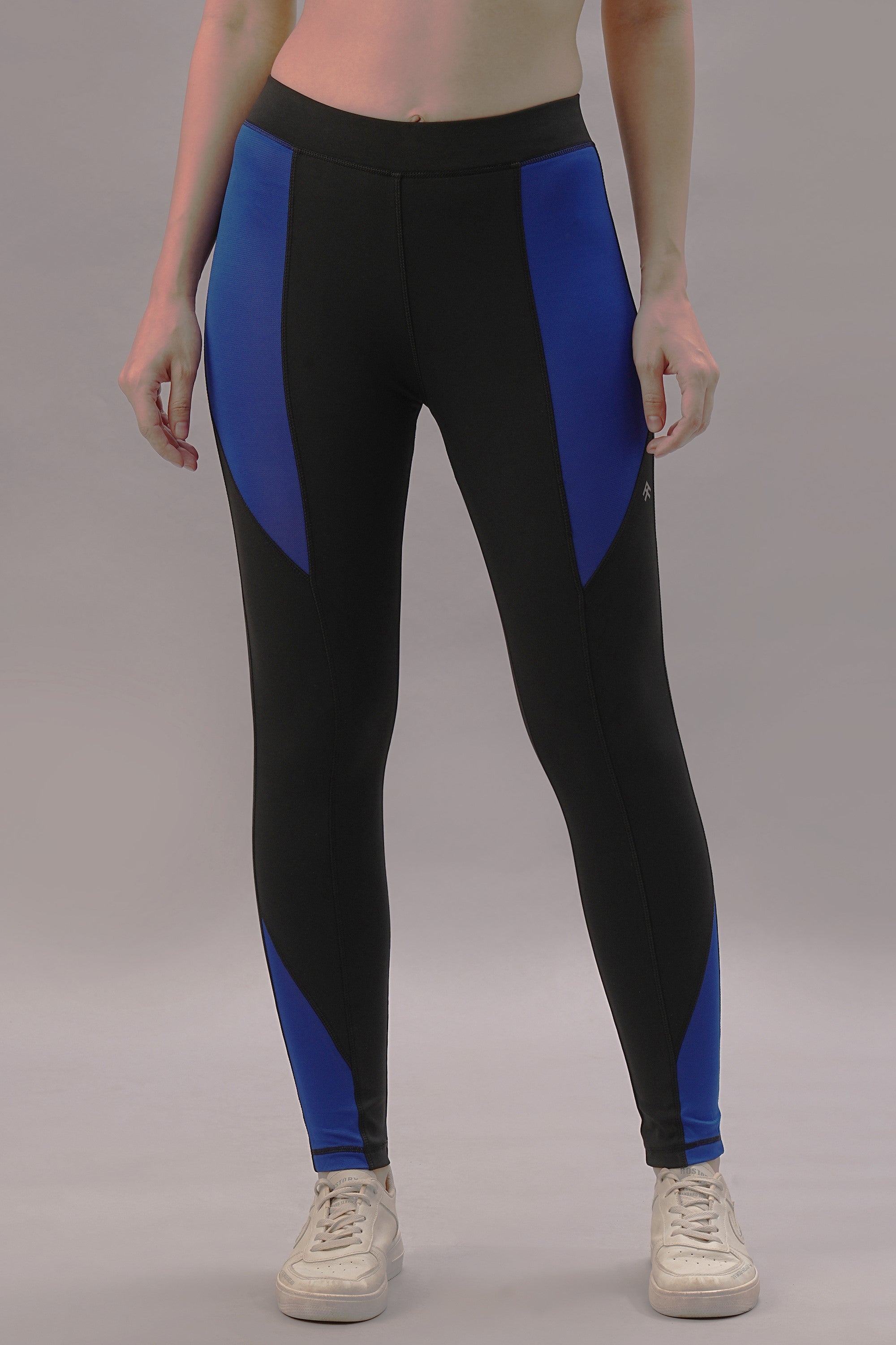 A woman stands against a plain background wearing the Black and Blue Pants, featuring a tailored fit with color-blocking design, paired with white sneakers.