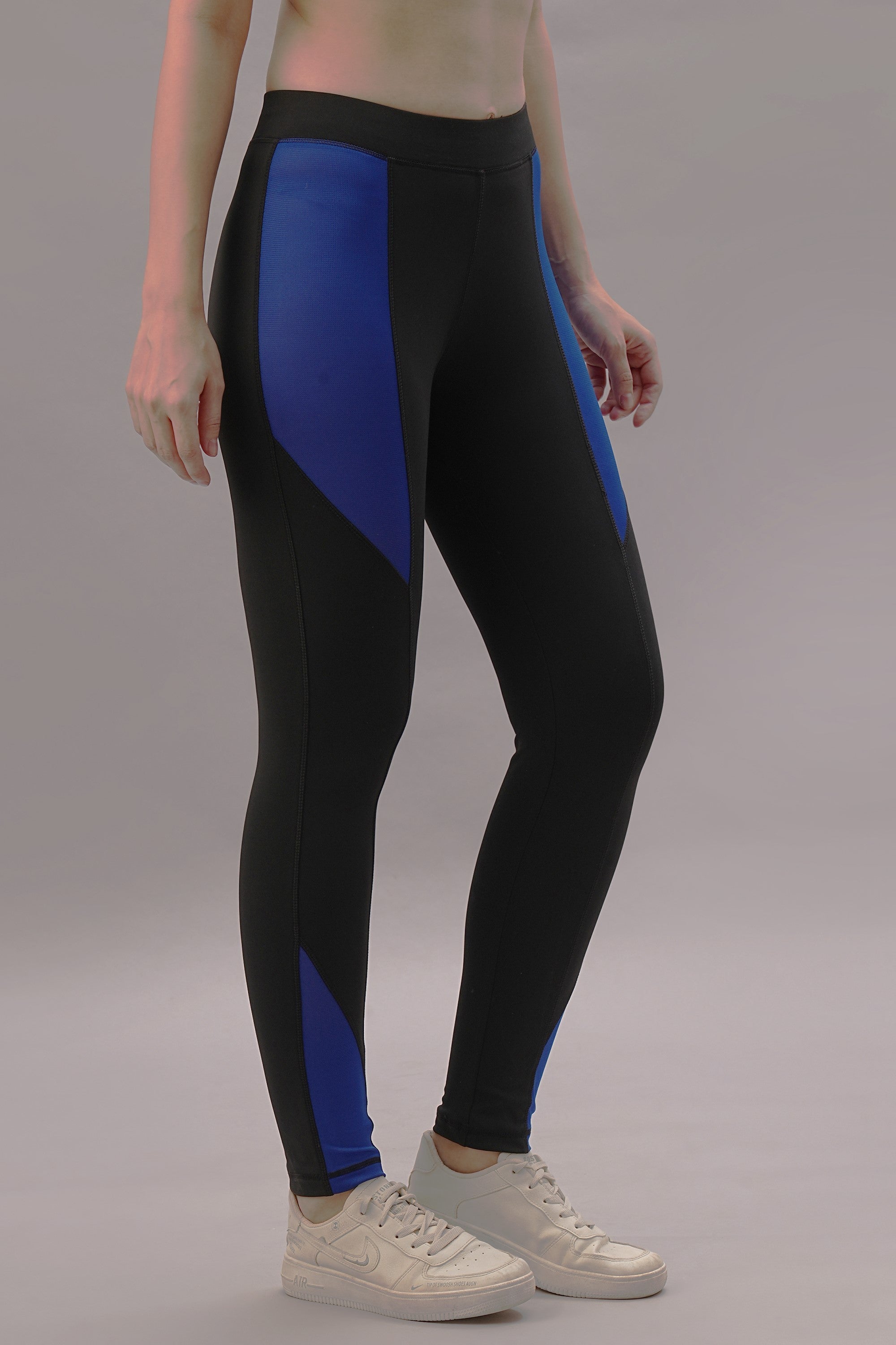 Model wearing Black and Blue Pants paired with white sneakers, standing against a gray background.