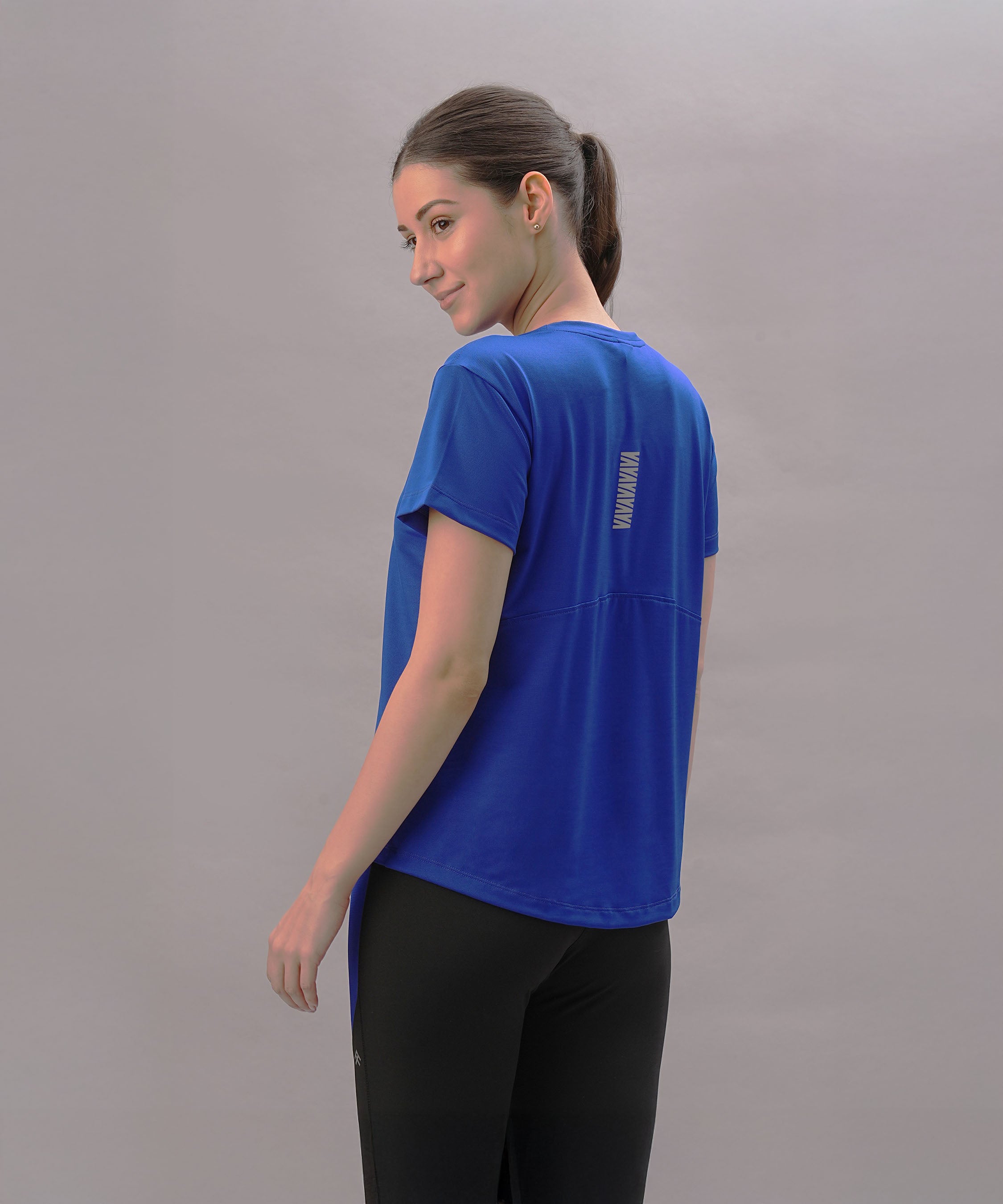 Woman wearing the Blue Comfort T-Shirt and black pants stands sideways, glancing over her shoulder against a light background—a stylish pick for an active lifestyle.