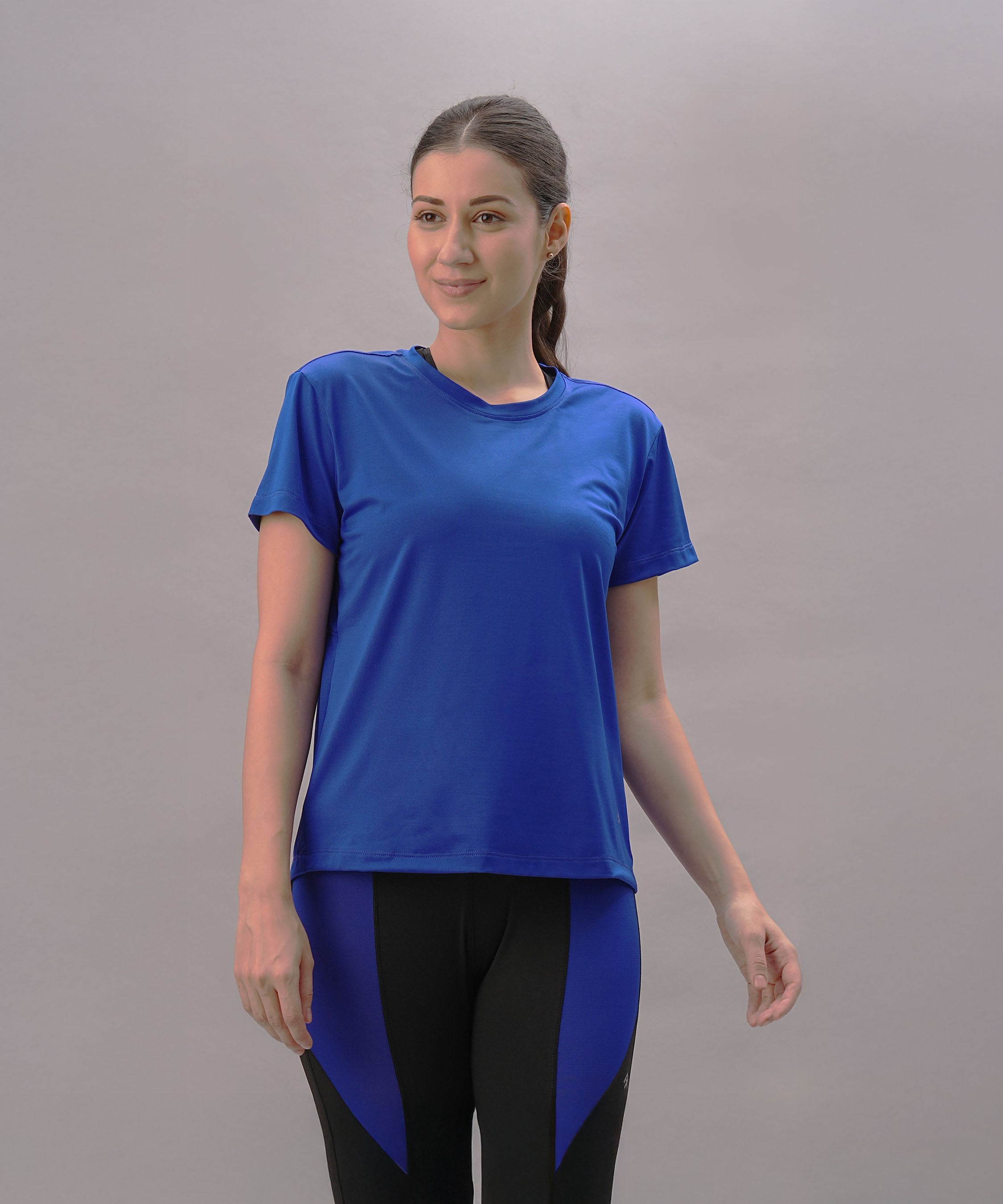 A woman wears the Blue Comfort T-Shirt and black leggings against a light gray background, showcasing an active lifestyle with the shirt's quick-drying fabric.