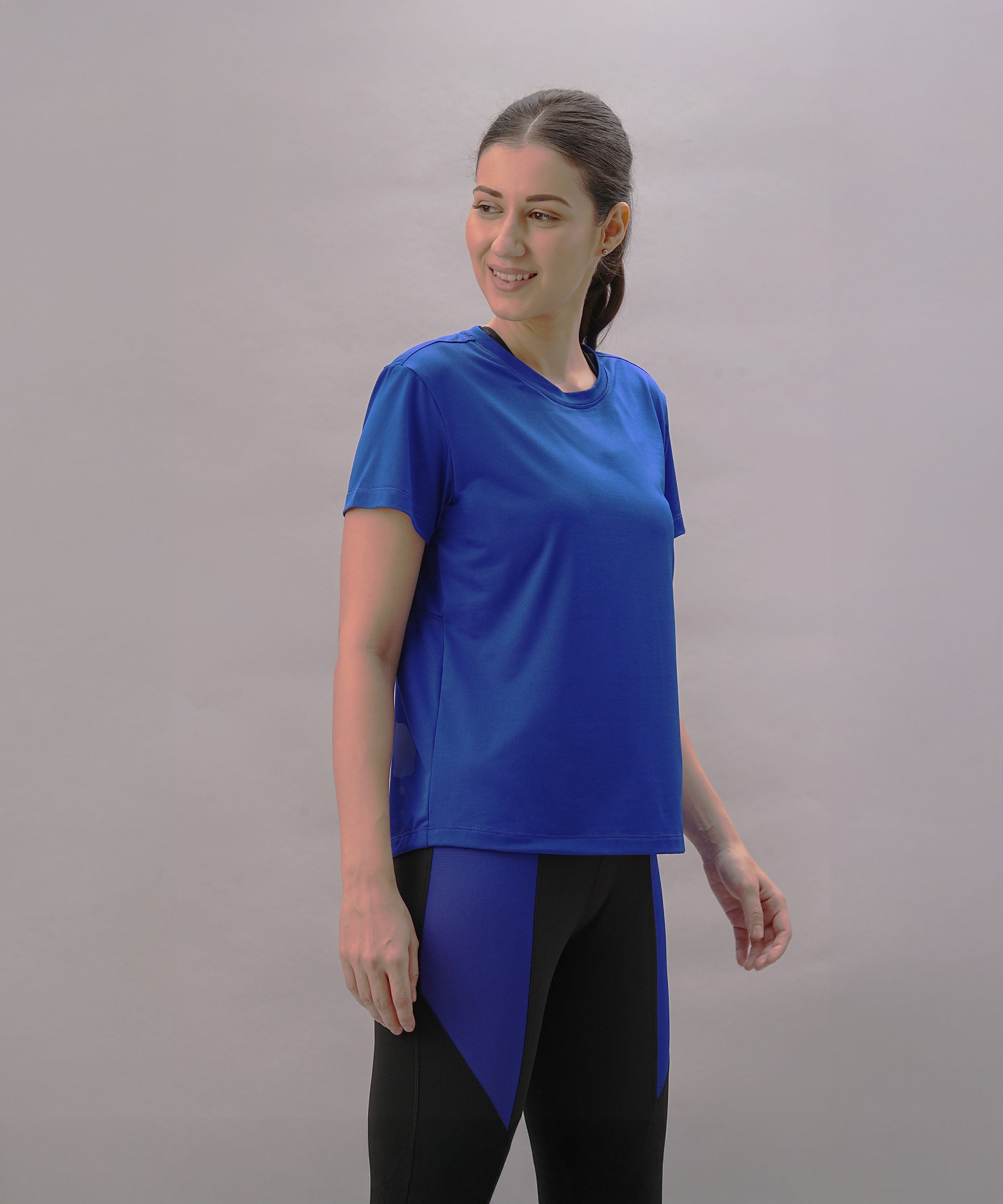 Woman wearing the Blue Comfort T-Shirt and black leggings with blue panels, smiling against a plain background—ideal for those with an active lifestyle.