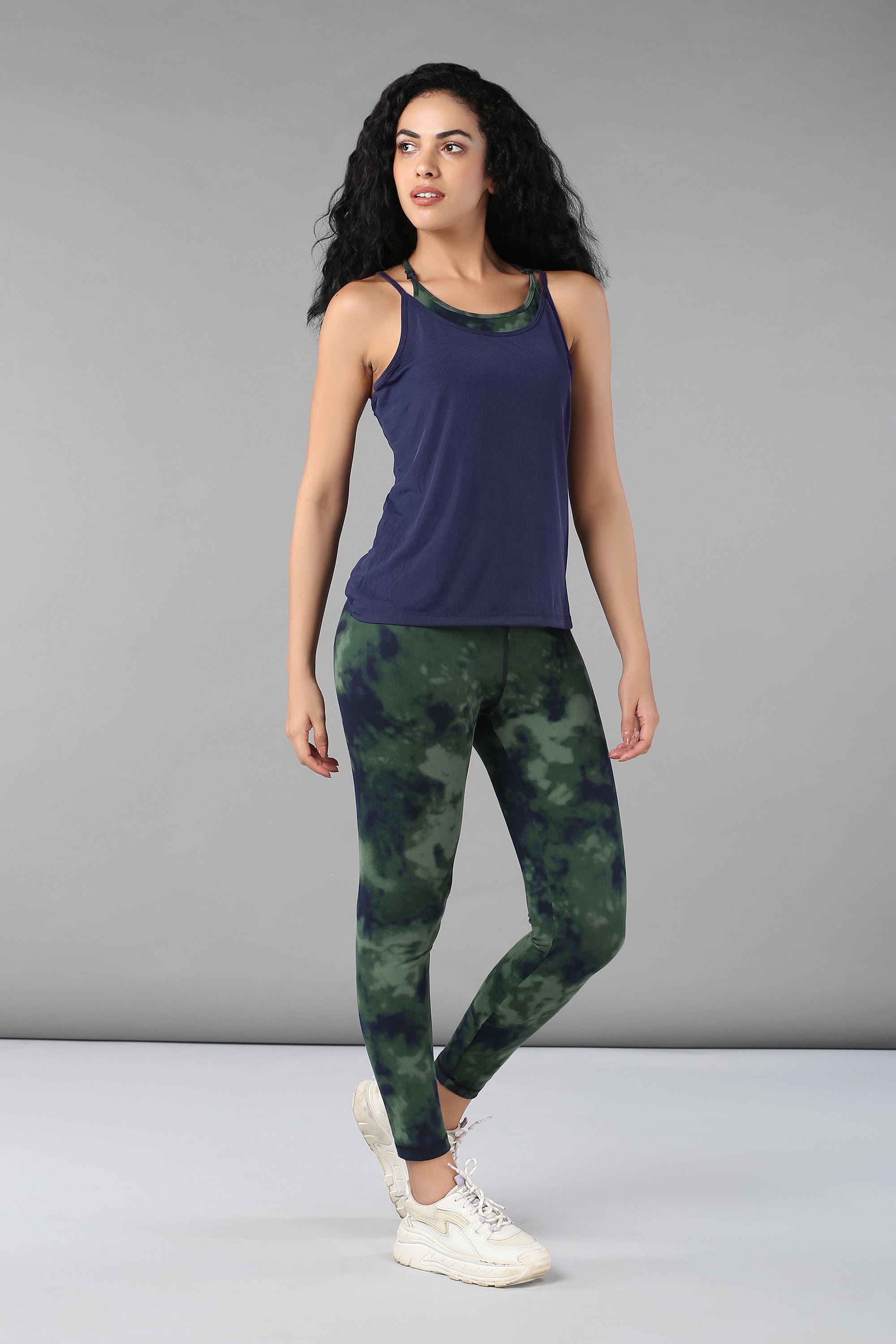 Woman wears a Tie & Dye Bra T shirt and green tie-dye leggings, standing against a plain gray background.