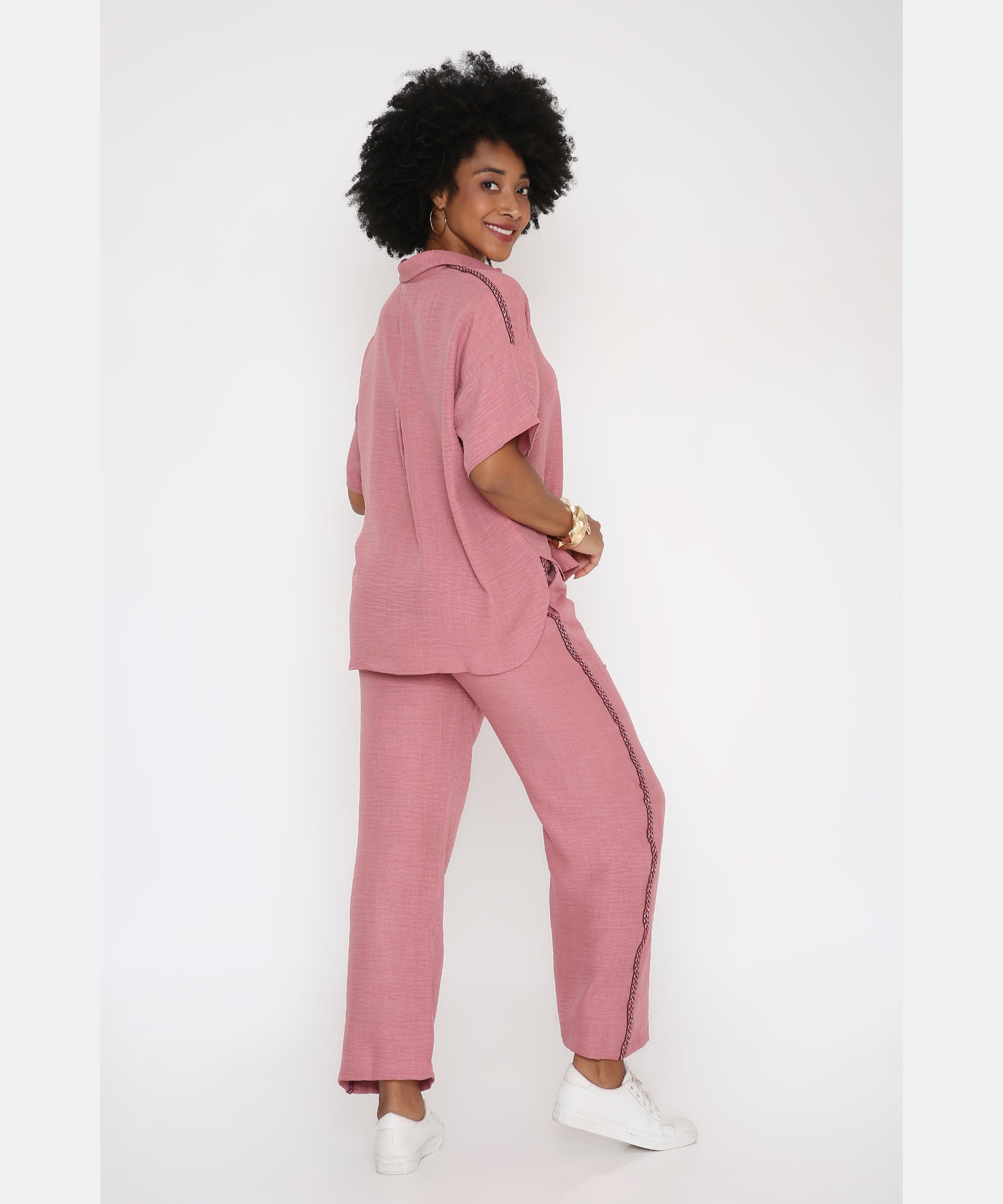 A woman smiles over her shoulder in the Vintage Pink Loose Shirt and Pant Cord Set with wide-leg pants and white sneakers, standing against a white background.