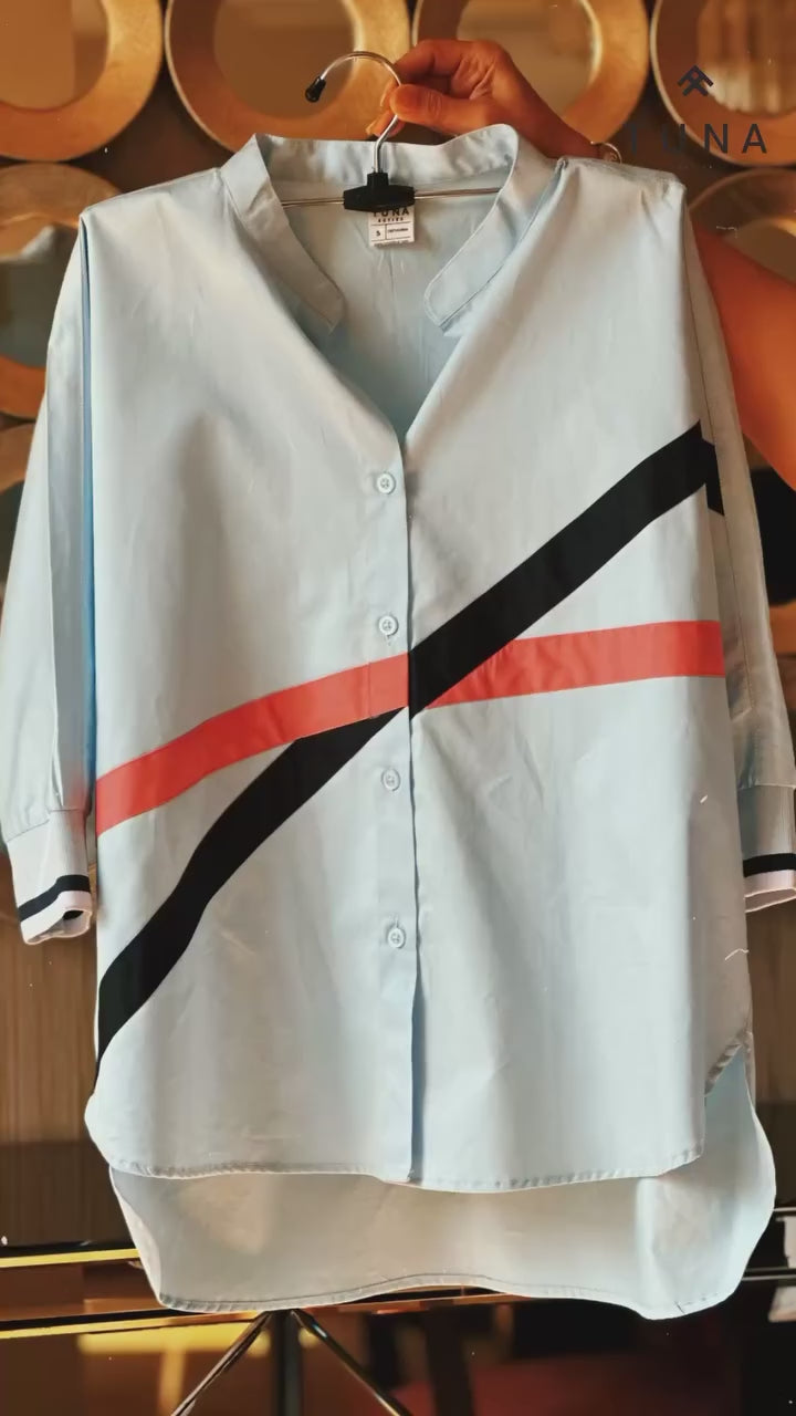 Load video: Woman in a light blue tracksuit with red and black stripes, standing indoors near plants and a mirror.