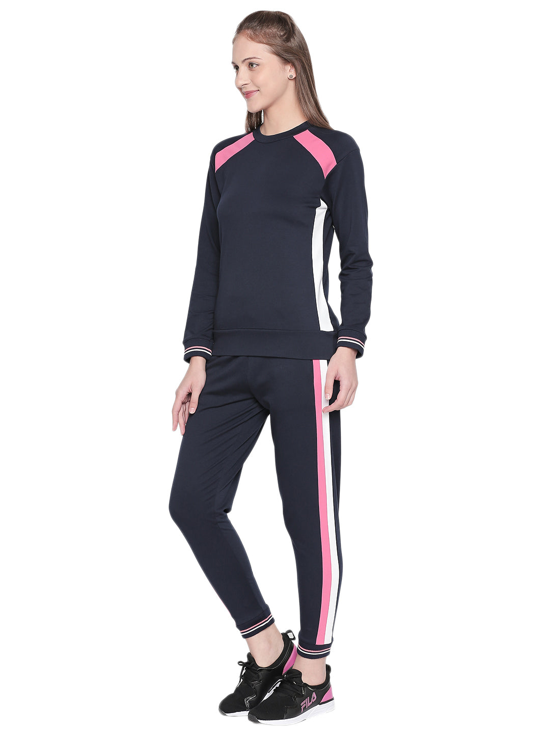A woman smiles, ready for a workout, wearing a full sleeve navy blue round neck sweatshirt from Tuna London with pink and white stripes.