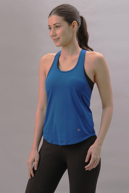 A woman wearing our Blue Racer Back Top from the activewear collection pairs it with black leggings, standing against a plain gray background and smiling, showcasing a sporty and stylish look.