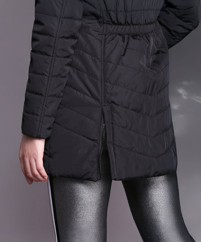 Person in a Black Fur Collar Long Puffer Jacket With Button and Zip Details, paired with shiny silver leggings, standing against a plain grey background.