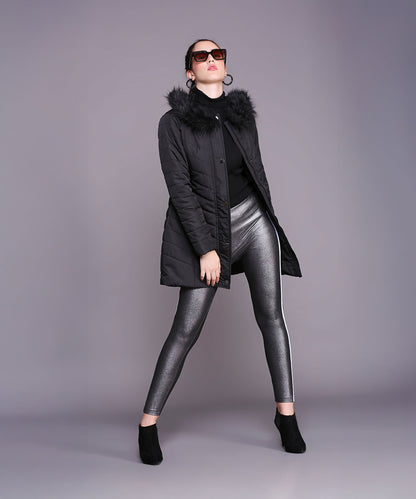 A woman confidently poses in a Black Fur Collar Long Puffer Jacket With Button and Zip Details, paired with metallic leggings, sunglasses, and ankle boots.