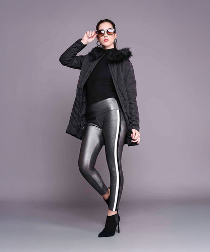 Woman in a Black Fur Collar Long Puffer Jacket With Button and Zip Details, metallic leggings, and sunglasses poses confidently against a plain gray background.