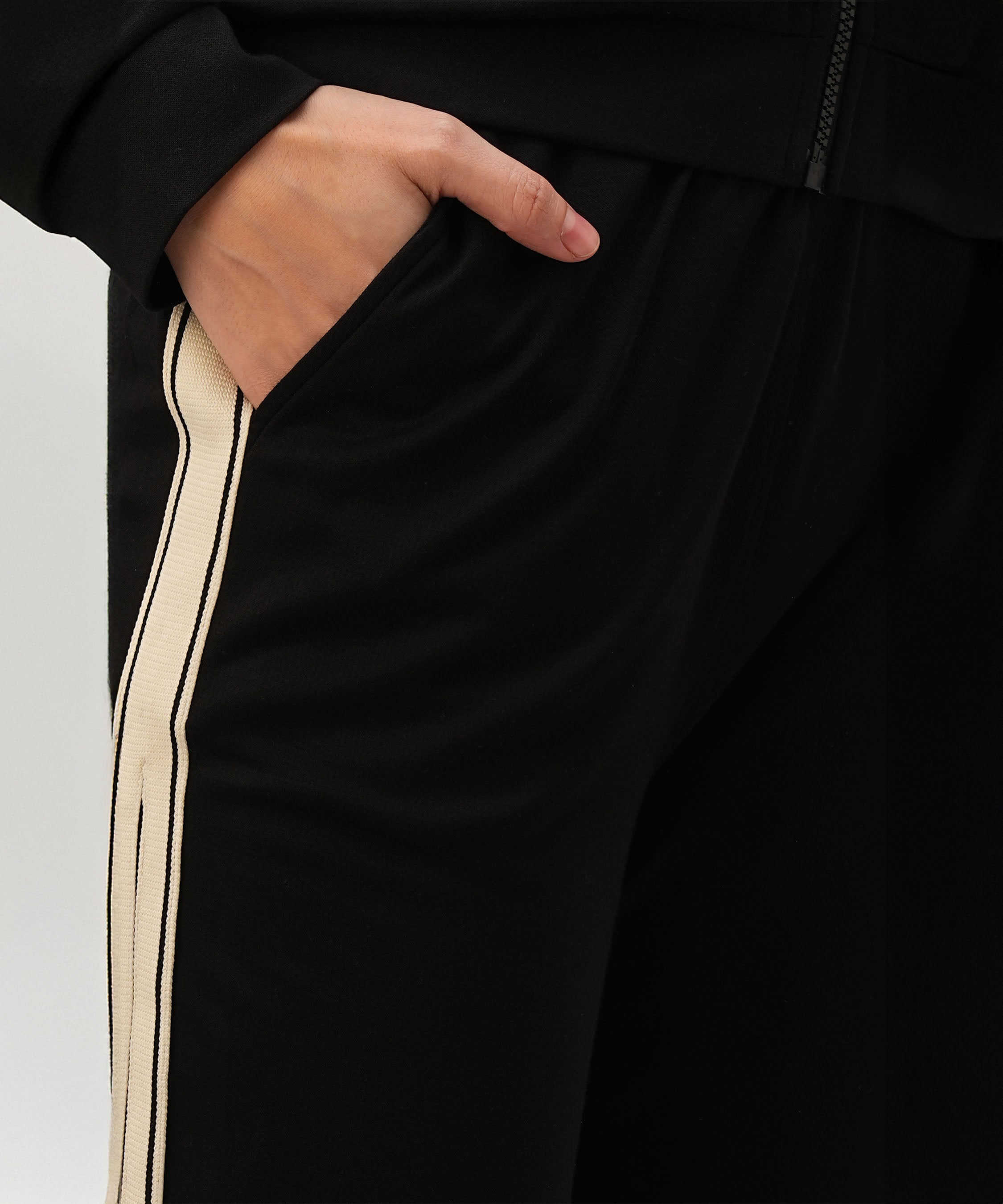 A person with their hand in the pocket of black pants with a white side stripe, styled as part of the Black Co-Ord Set made from soft cotton lycra.