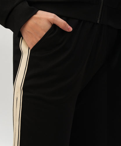 A person with their hand in the pocket of black pants with a white side stripe, styled as part of the Black Co-Ord Set made from soft cotton lycra.