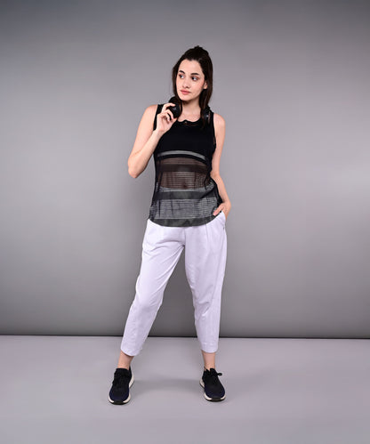 A woman in athletic wear poses against a gray background, holding sunglasses and with one hand in her pocket, showcasing the Pleated Yoga Pant With Smocked Waistband.