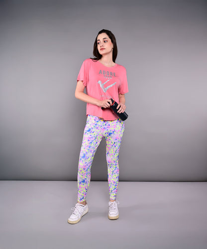 Woman in an 'Adore Your Core' printed tee and colorful leggings holds a water bottle, standing against a gray background.