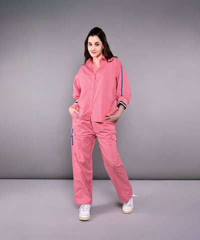 Woman wearing the Effortlessly Chic Set—a pink cotton co-ord with a batwing sleeve shirt and cargo track pants—stands with hands in pockets against a plain gray background.