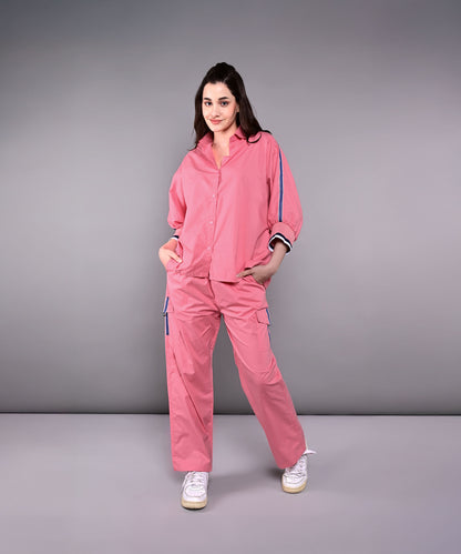 Woman wearing the Effortlessly Chic Set—a pink cotton co-ord with a batwing sleeve shirt and cargo track pants—stands with hands in pockets against a plain gray background.
