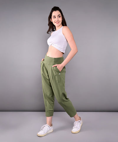 Woman poses confidently in a White Twisted Crop Top, paired with green pants and white sneakers, against a gray background.
