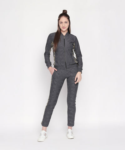Woman in a Camouflage Print Tracksuit with dark grey elasticated track pants, gold detailing, and a V-neck collar jacket, standing and smiling against a white background.