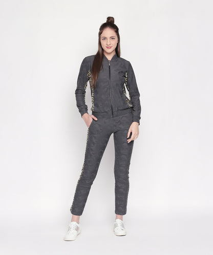 Woman in a Camouflage Print Tracksuit with dark grey elasticated track pants, gold detailing, and a V-neck collar jacket, standing and smiling against a white background.