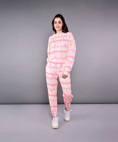 Woman in the Comfort Fit Tie-Dye Sweatshirt With Joggers Set, paired with white sneakers, stands and smiles against a gray background.