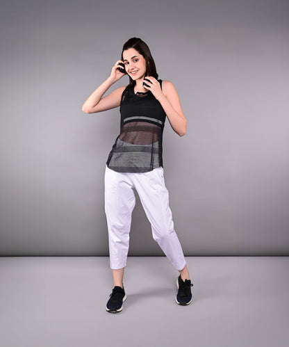 Woman smiles and poses in the Tuna Active Black Netted Tank Top with white pants against a plain gray background.
