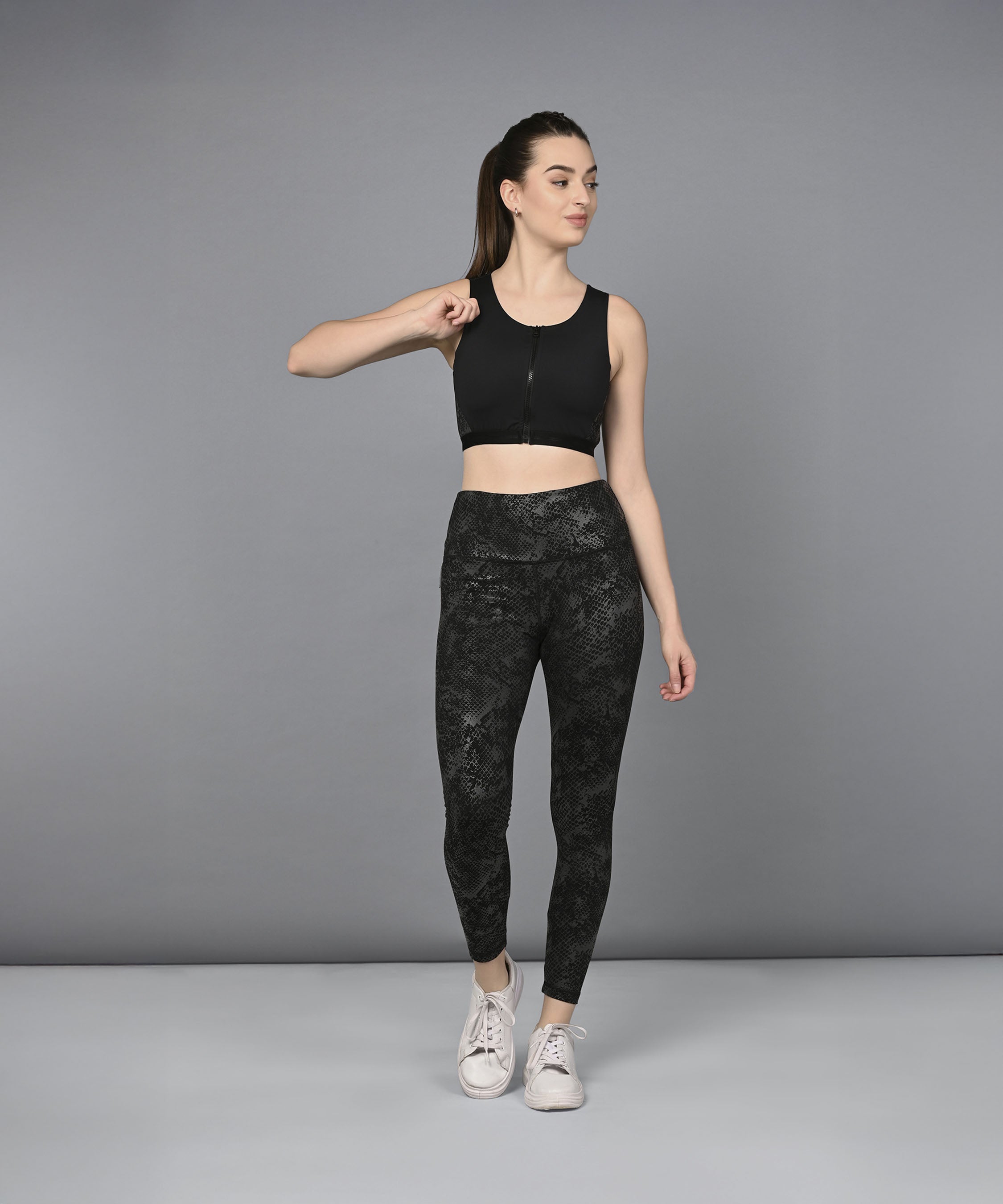 A woman models the Zipped Sports Bra and Metallic Legging, standing against a gray background and looking to the side.