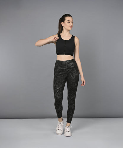 A woman models the Zipped Sports Bra and Metallic Legging, standing against a gray background and looking to the side.